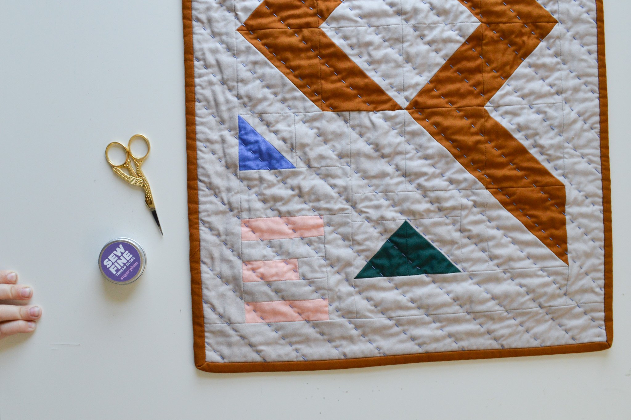  a modern wall hanging that is hand quilted on a table with some quilting notions 