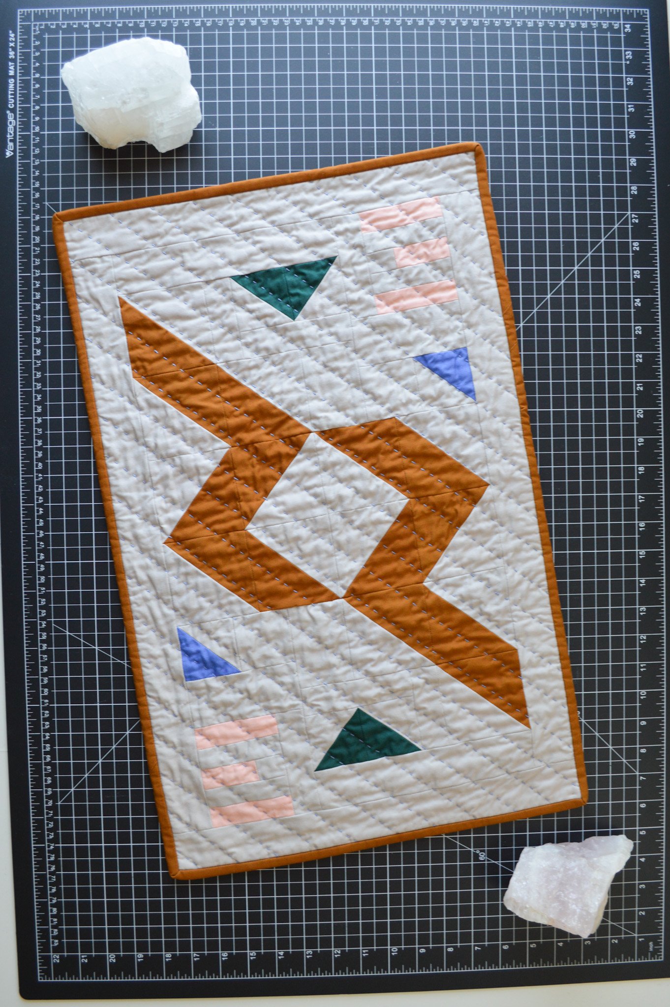  a hand quilting modern mini quilt and some crystals on a black cutting mat 