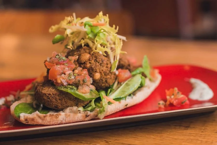 Veggie burger met falafel, sla, tomaat en saus op een rode plaat
