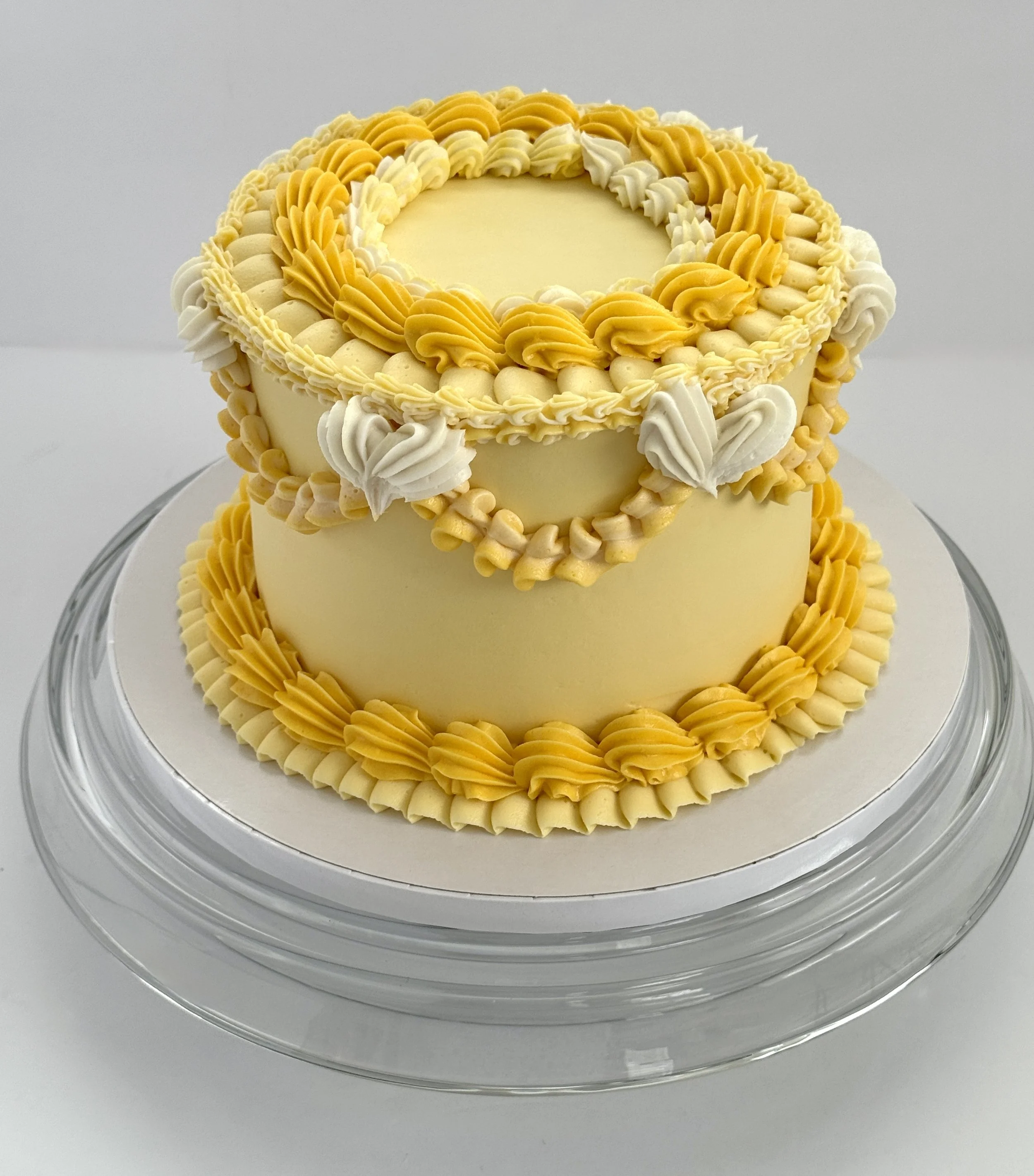 A tiered cake decorated with yellow and white piping, featuring a circular pattern around the top and layered design.