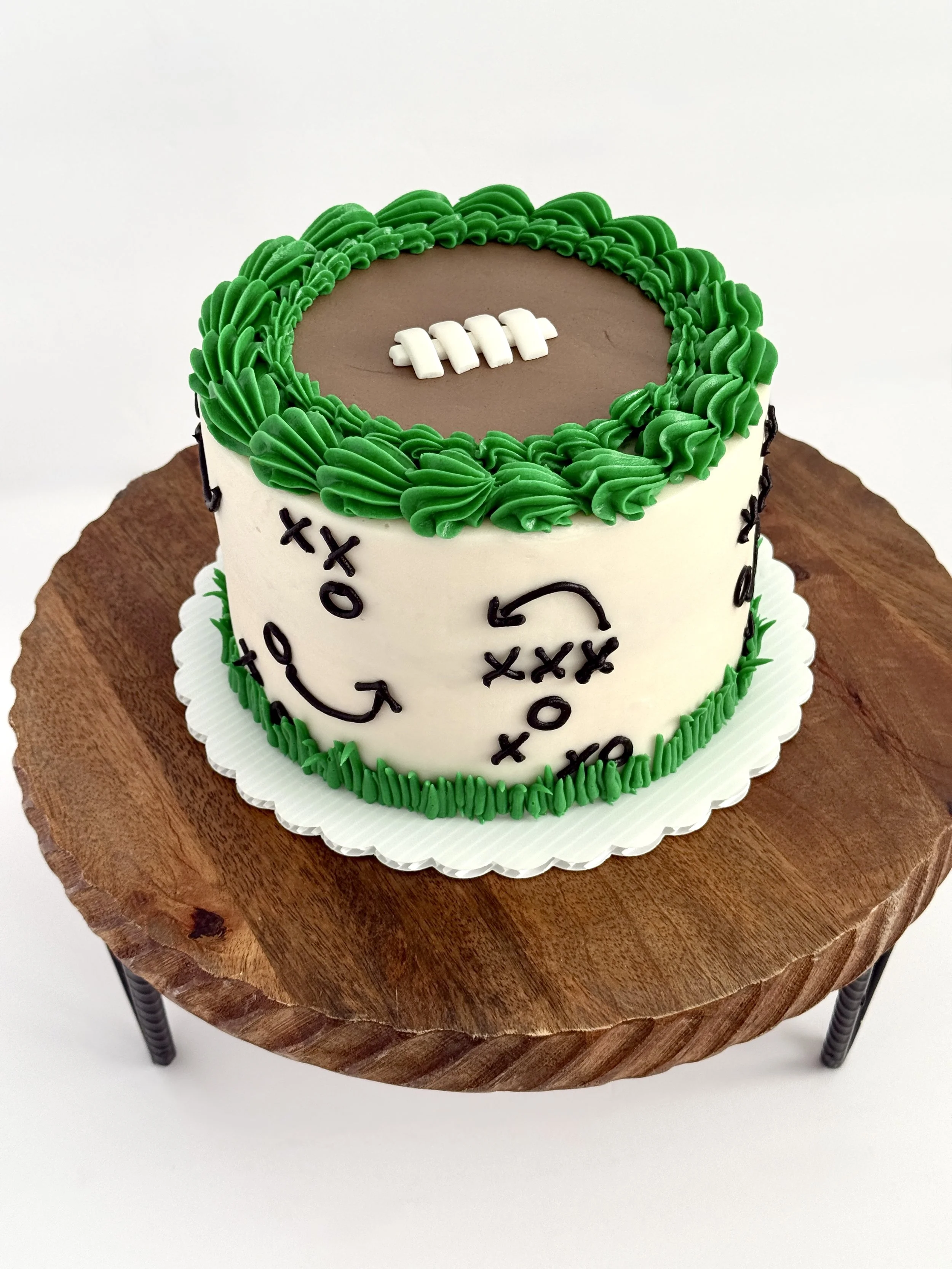 Birthday cake decorated with green and white icing, resembling a sports theme, placed on a wooden table.