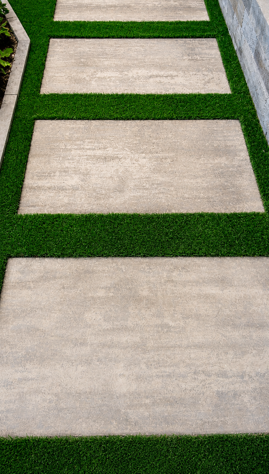 Close-up of clean artificial turf strips installed between large concrete pavers for a modern backyard walkway.