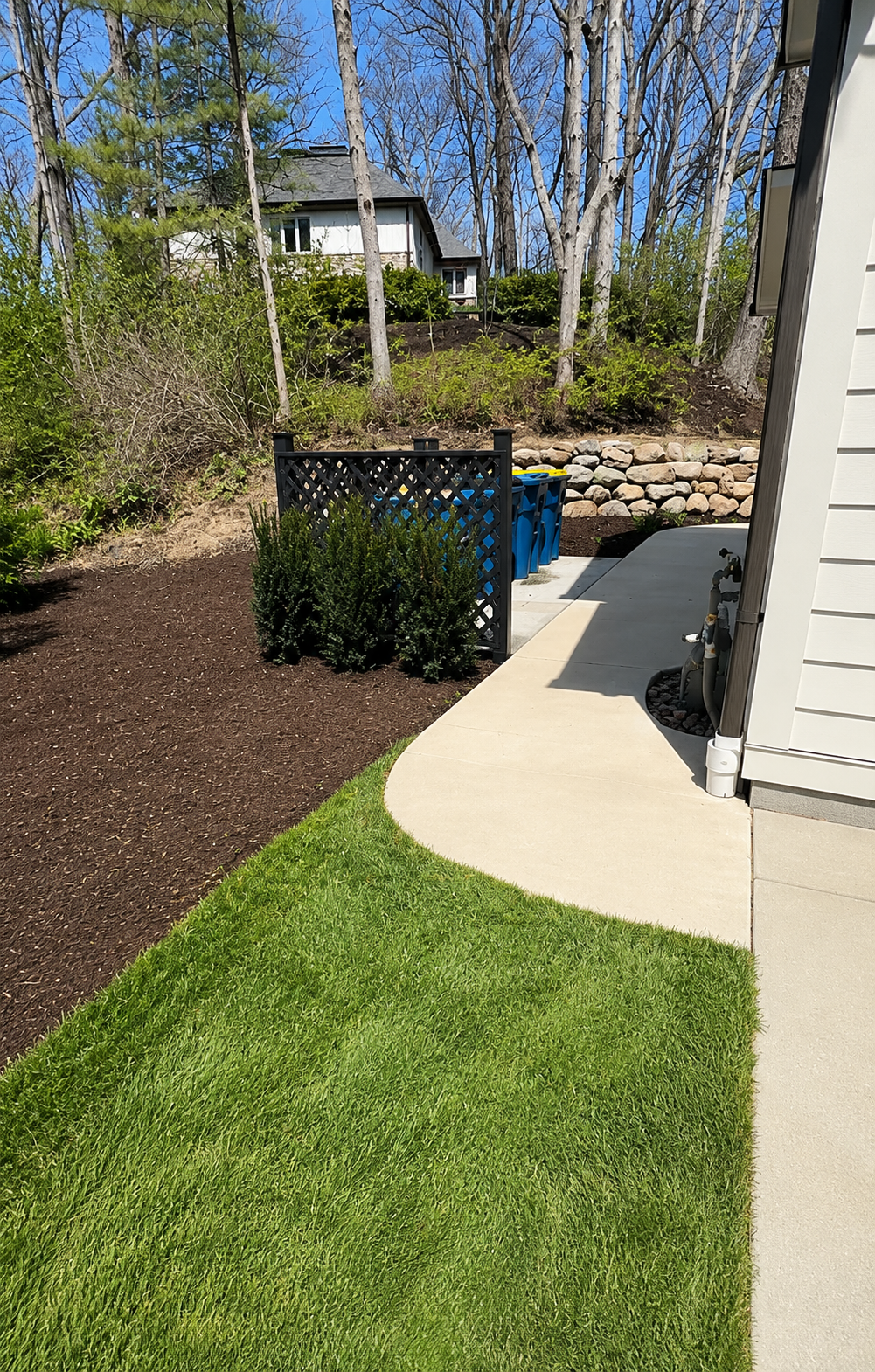 Newly installed concrete sidewalk in a residential backyard with fresh landscaping and retaining wall