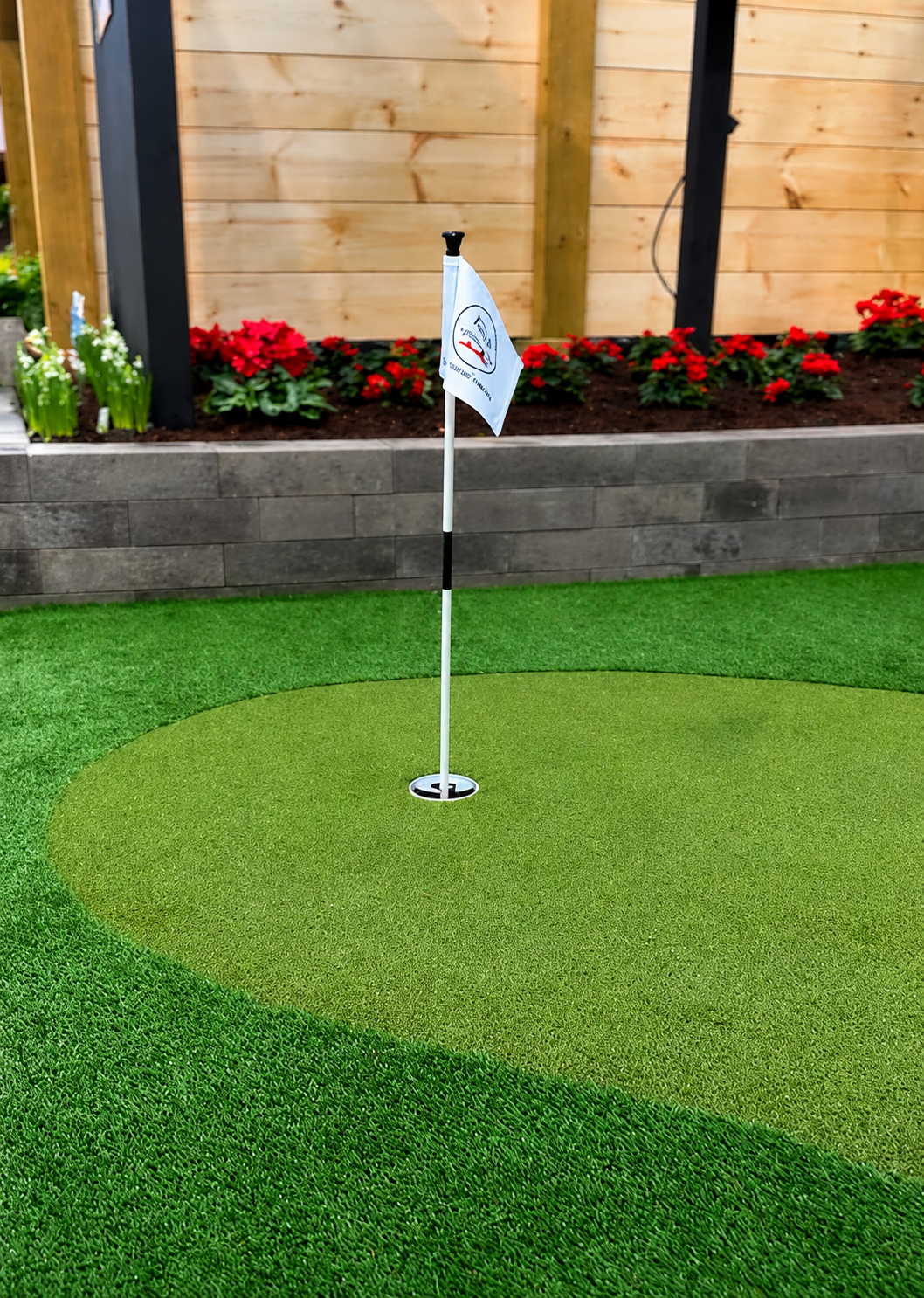 Close-up of a professional artificial turf putting green cup and pin flag installed in a residential backyard.