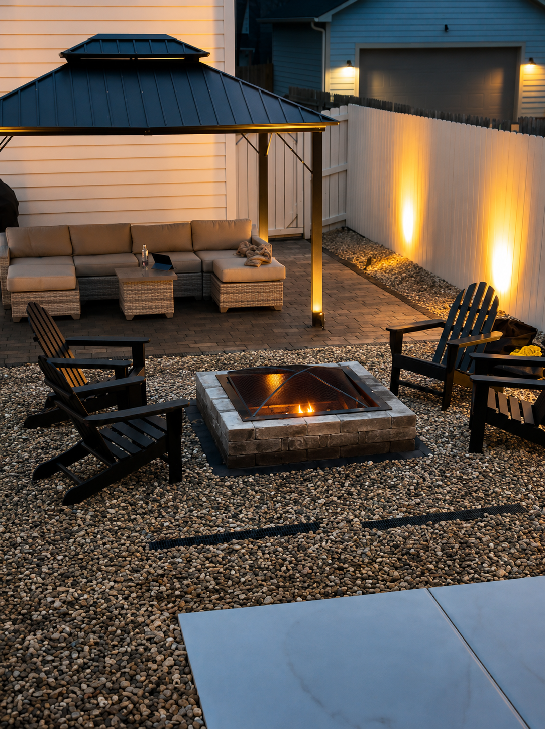 Cozy evening backyard patio installation featuring a burning fire pit, gravel landscaping, and modern outdoor fence lighting.