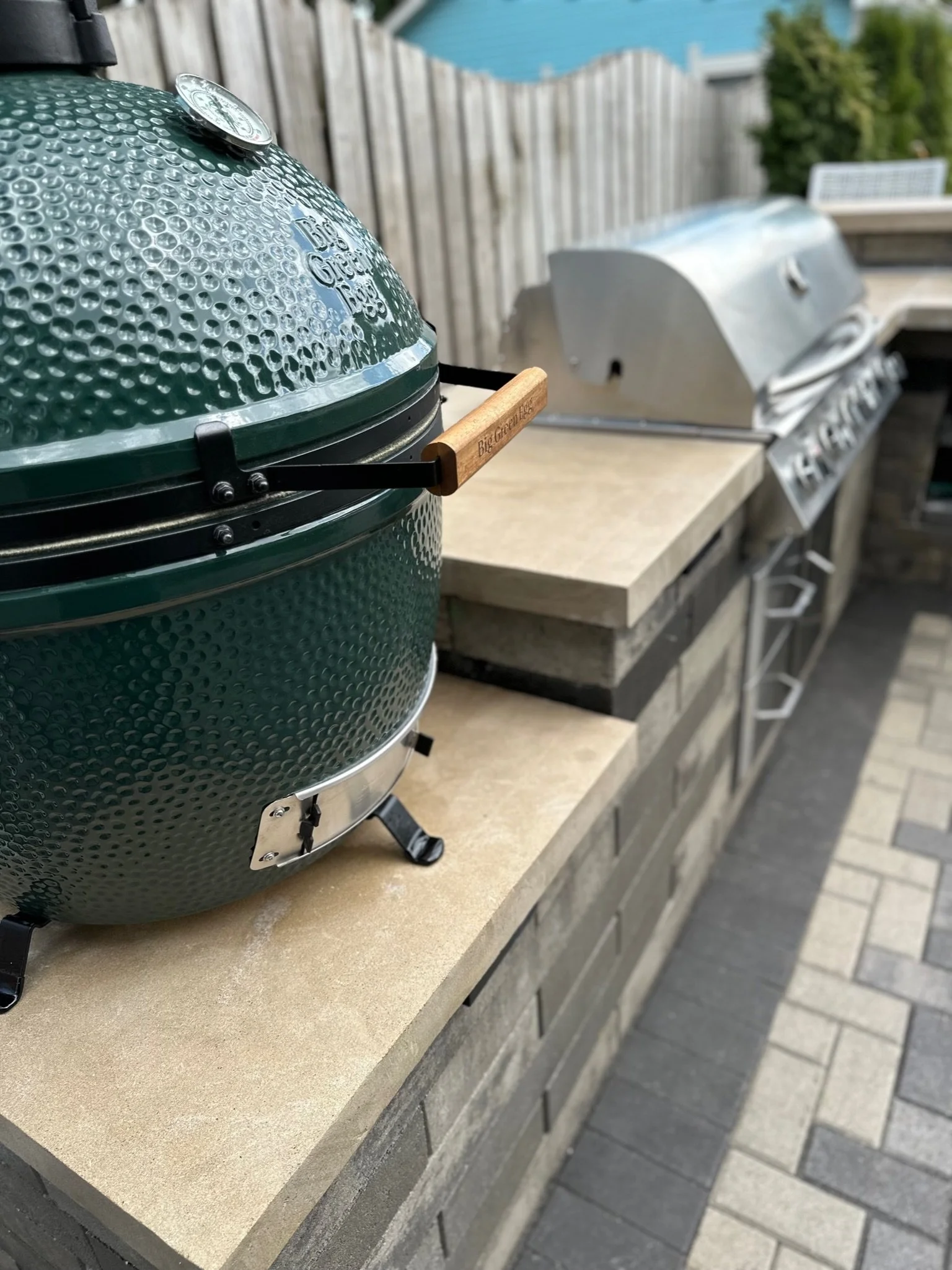 Custom masonry outdoor kitchen by B&F Landscaping featuring an integrated Big Green Egg smoker and a built-in stainless steel gas grill on premium stone countertops and a paver patio.