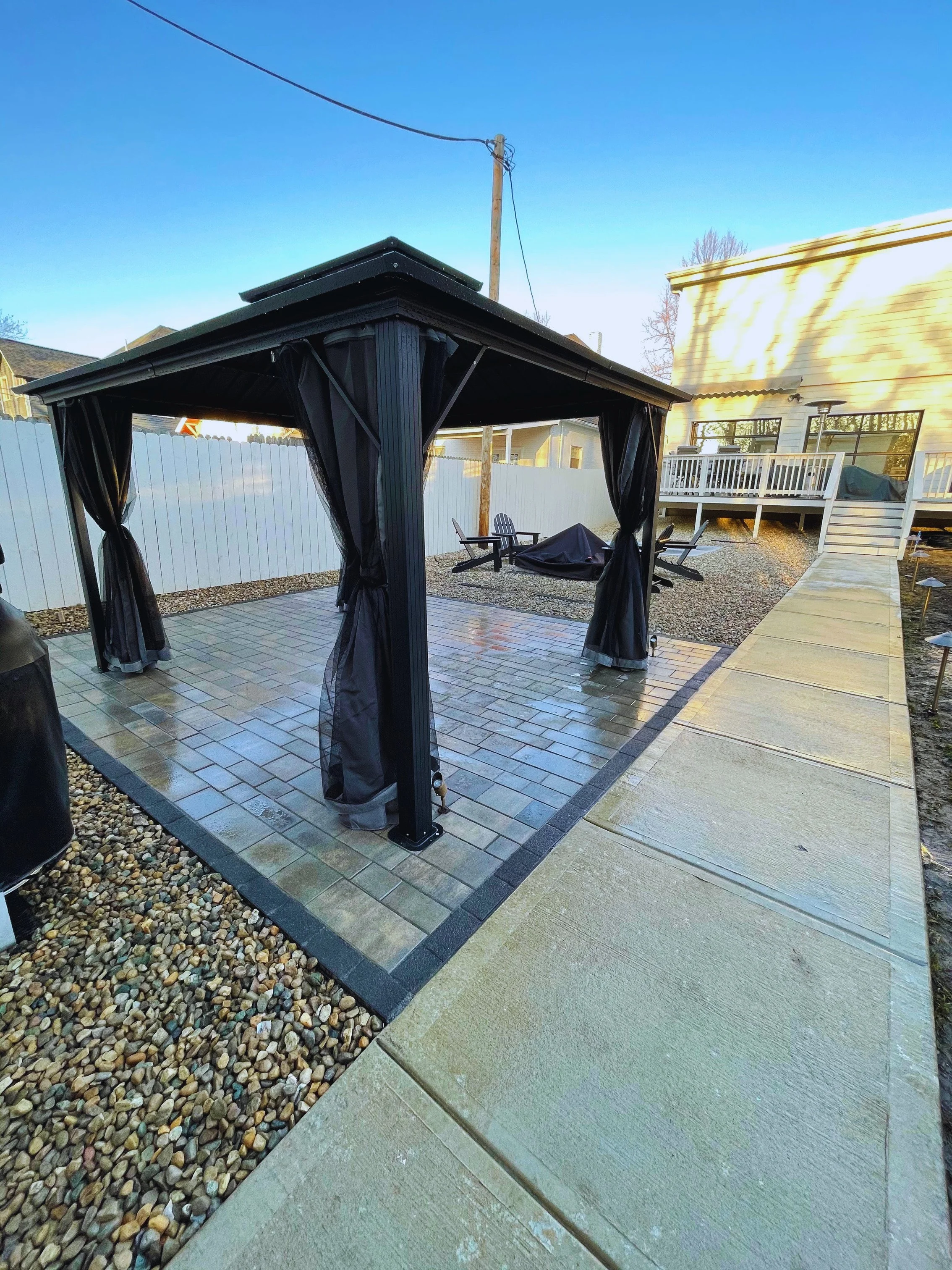 Freestanding black louvered pergola with integrated mosquito netting, professionally installed on a custom paver patio extension by B&F Landscaping.