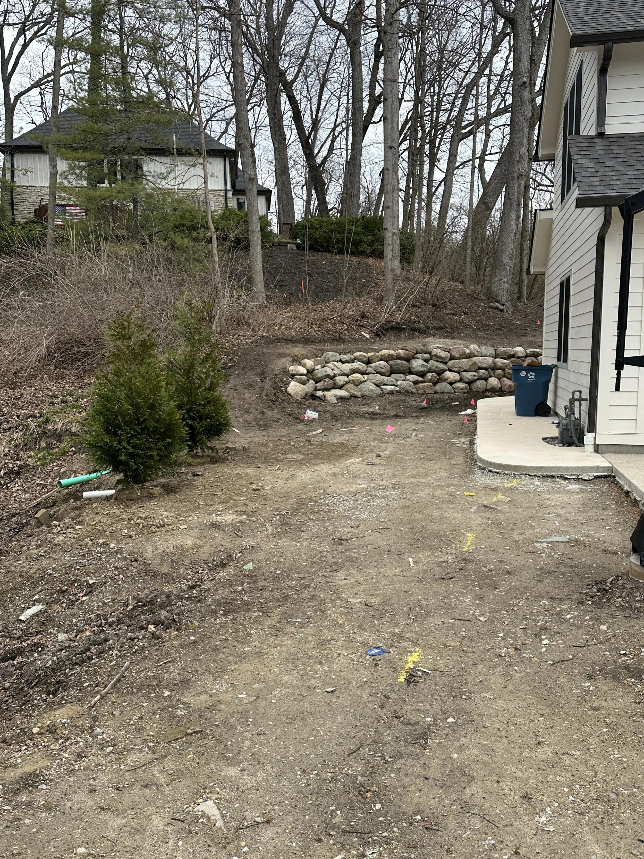 Before concrete sidewalk installation in a residential backyard with unfinished grading and retaining wall.