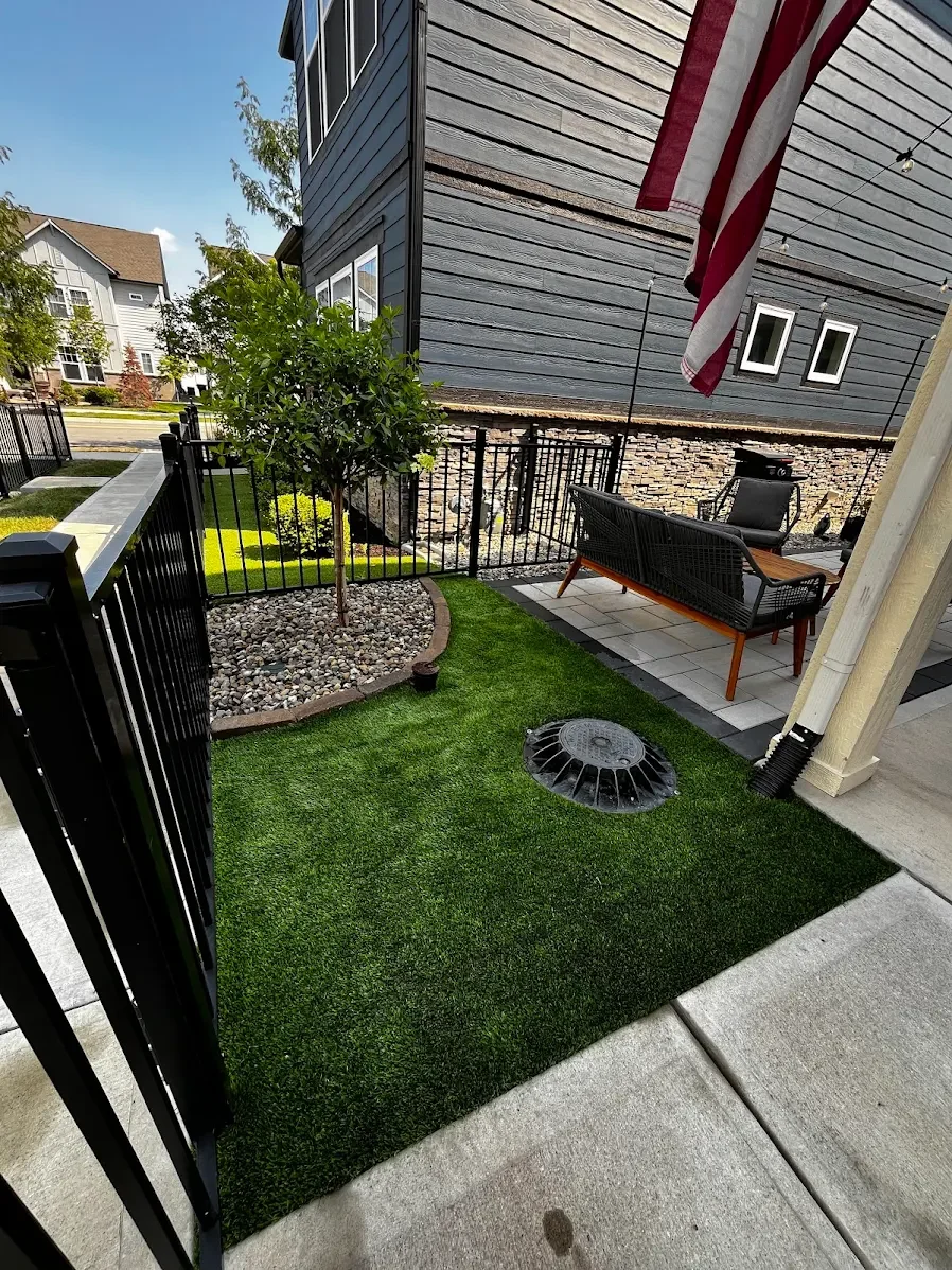 Small backyard landscaping featuring river rock mulch, a young tree, and turf integration by B&F Landscaping