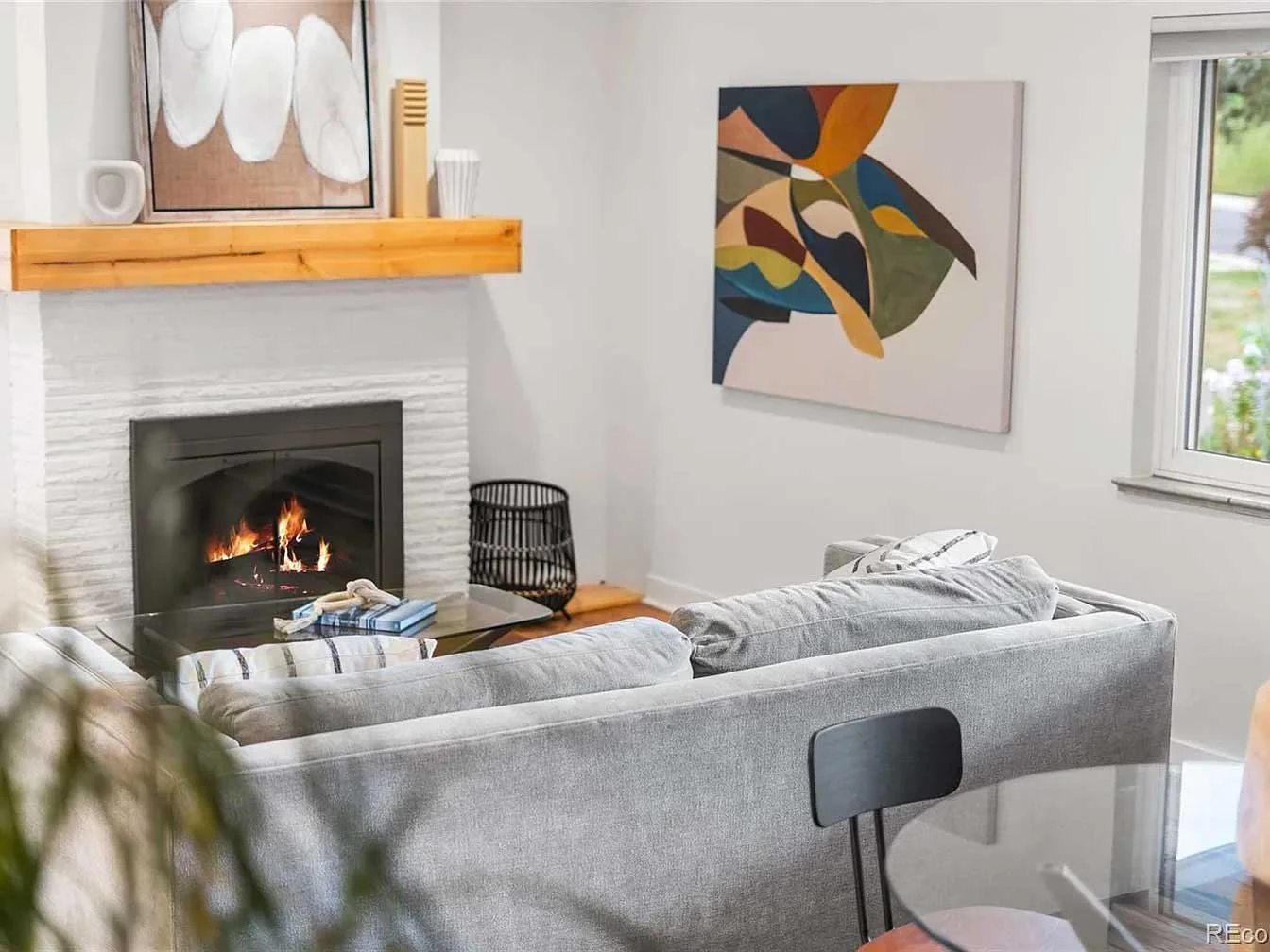 Cozy Denver luxury home staging of modern living room with lit fireplace, gray sofa, abstract art, wooden shelf, and sculptural pieces.