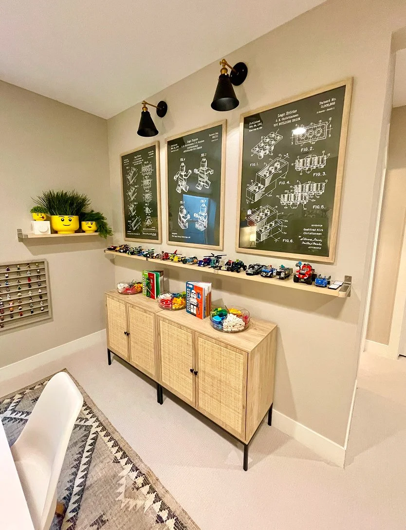 Stylish play space from full service interior design firm, showcasing wall-mounted invention blueprints, yellow plant, toy cars on shelf, and woven cabinet on rug.