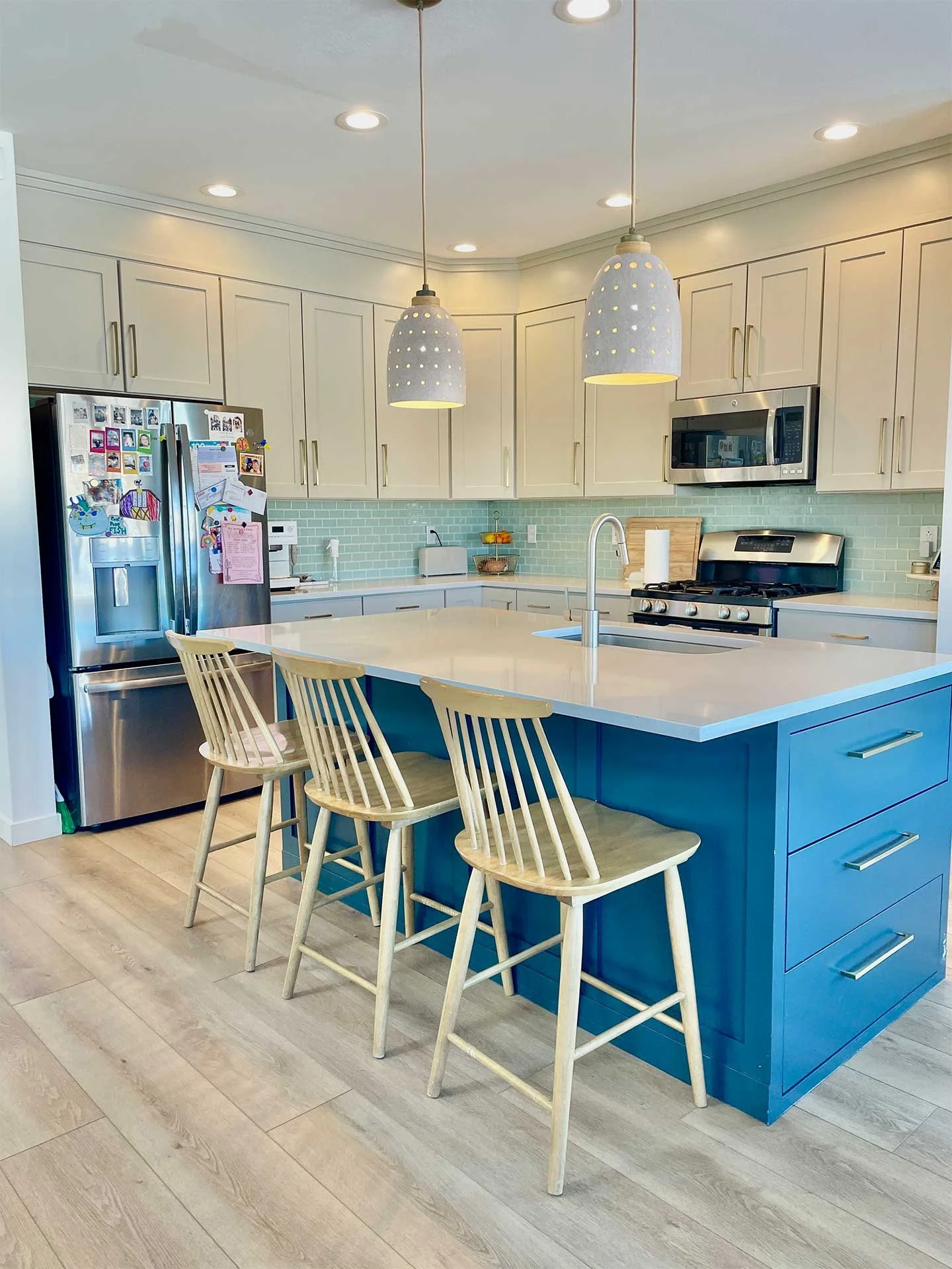 Contemporary kitchen island in blue with white cabinets, stools, green tiles, showcasing professional interior design services.