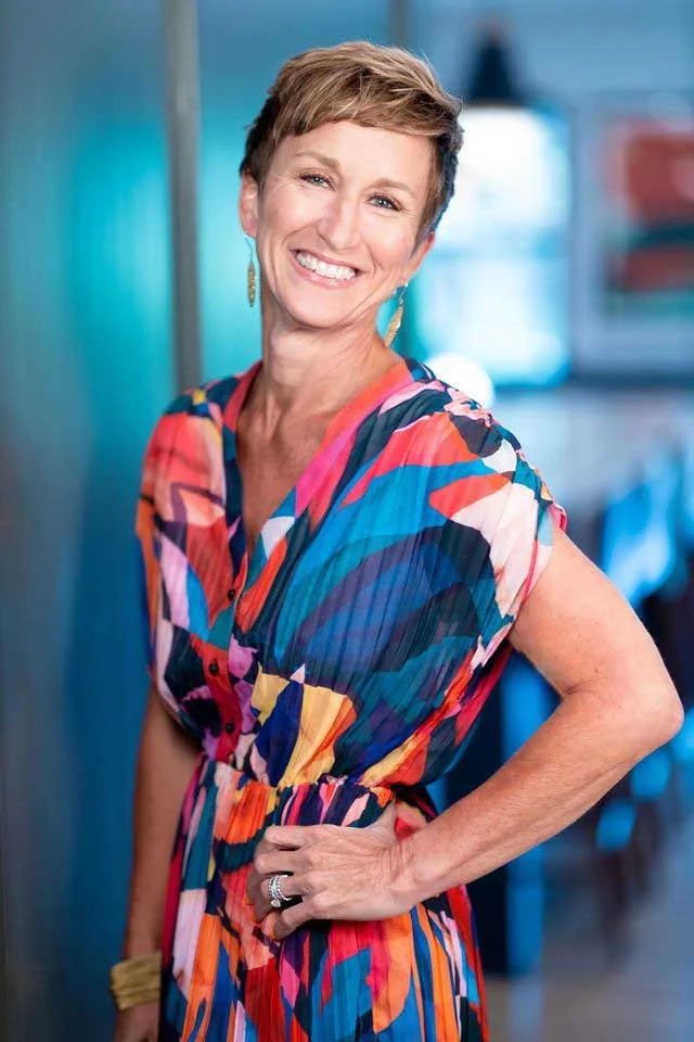 Professional headshot of smiling Jen Kurtz, Interior Designer in Denver CO, in multicolored dress amid stylish office decor.