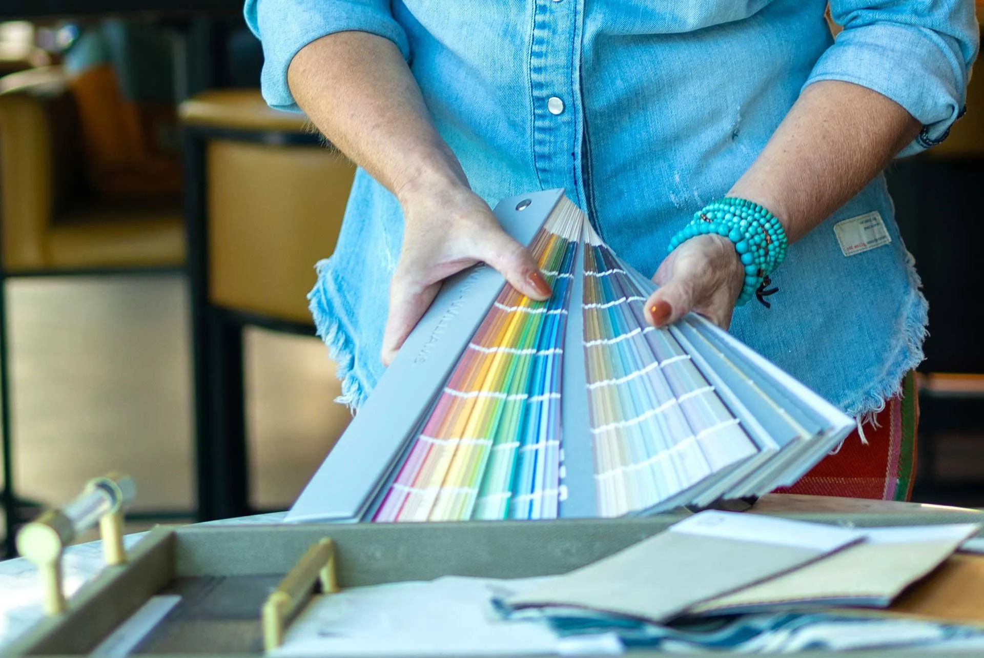 Woman's hands holding a multicolored paint swatch fan for paint color consulting, turquoise bracelets visible on wrists.