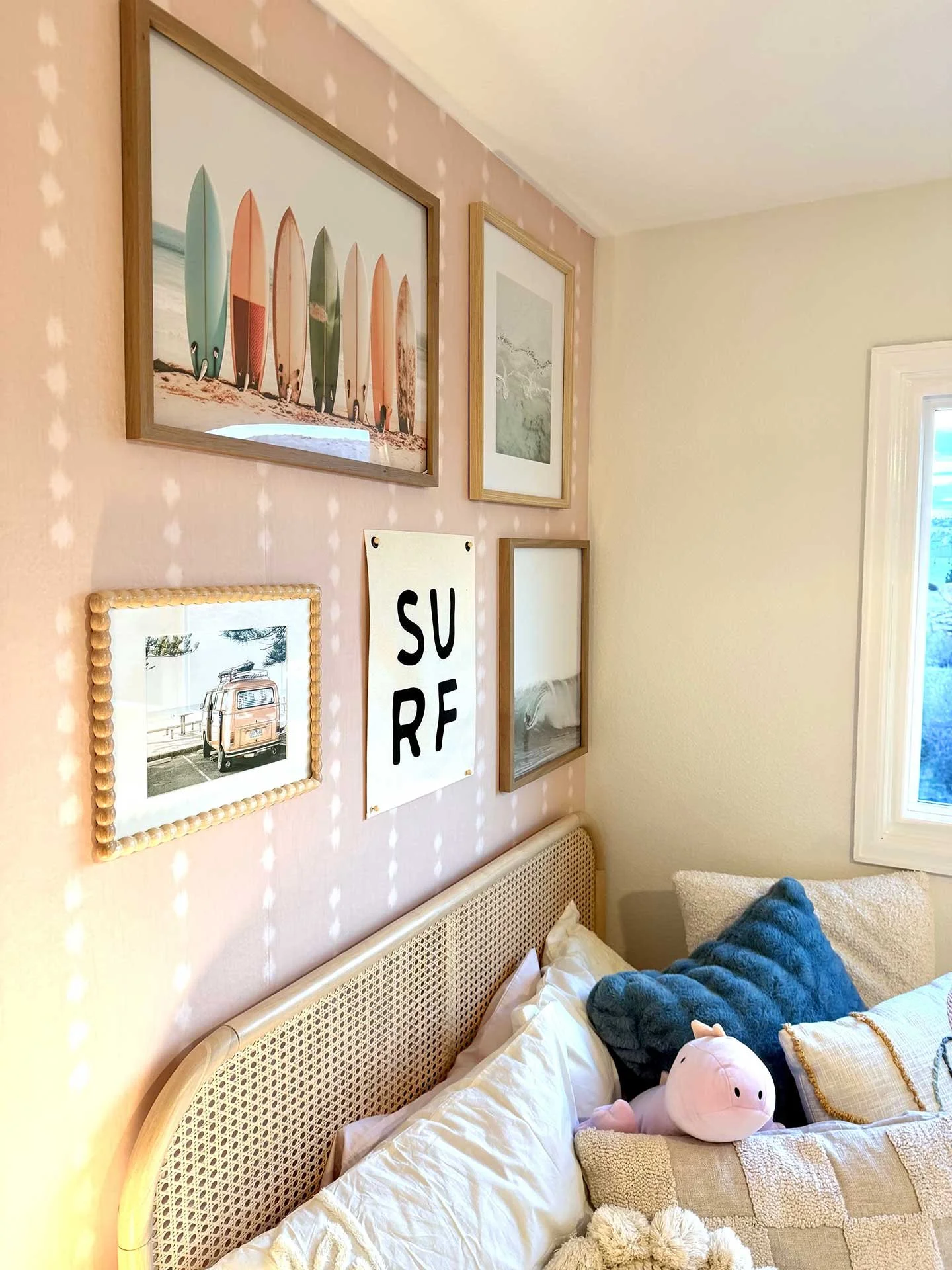 Close-up of teen bedroom gallery wall with beach-themed artwork above a rattan headboard, styled with layered pillows in soft, coastal tones.