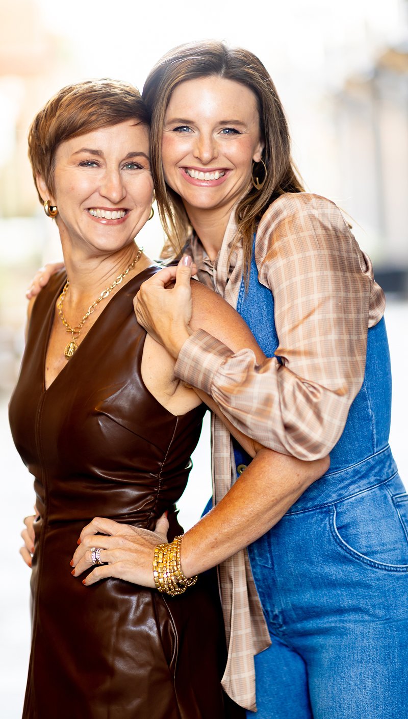 Jen and Katie of Denver's full service interior design firm hug happily outside, showcasing residential design expertise.