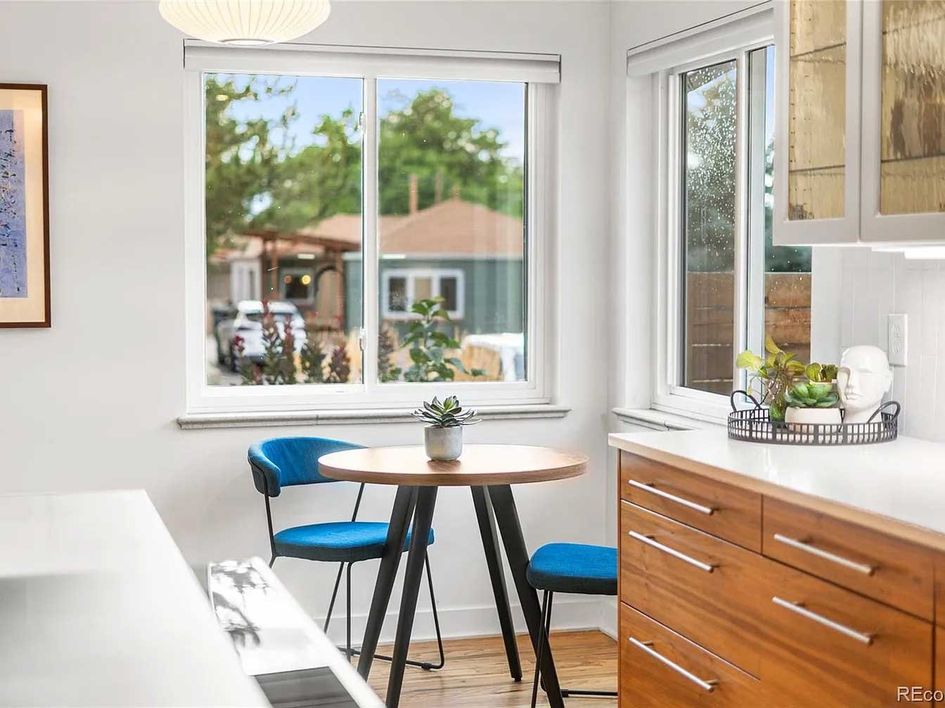 Premium home staging in a modern kitchen featuring blue upholstered chairs, round wooden table with succulent, plants, and sunny window.