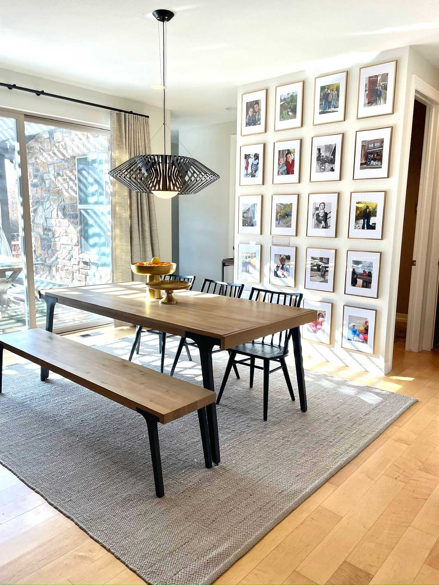 Elegant luxury interior design of sun-filled dining room with rectangular oak table, black chairs and bench, spiky pendant fixture, and partitioned photo wall display.