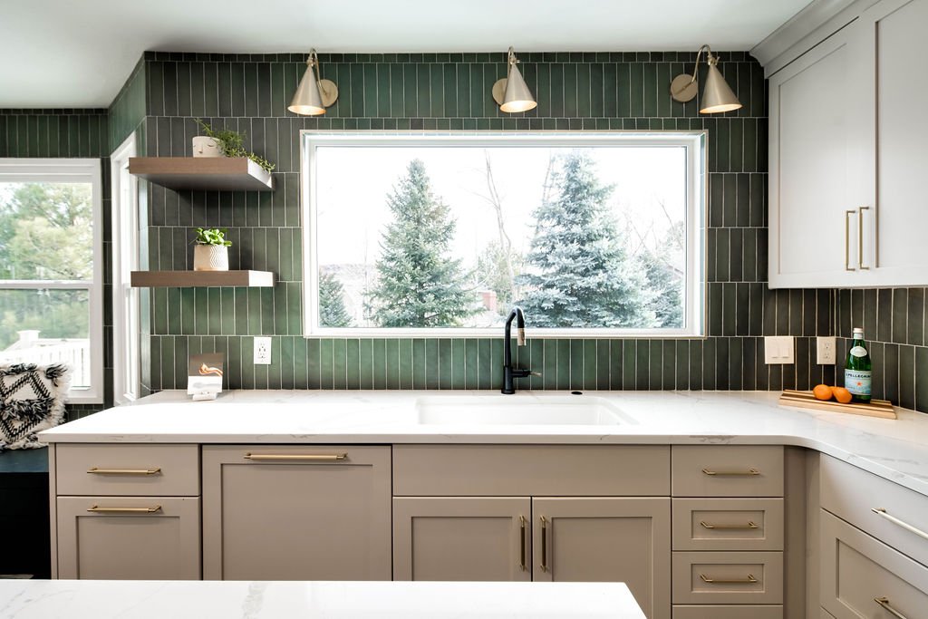 Sleek remodel renovation showcasing green tiled backsplash, matte black gooseneck faucet, beige cabinets, and natural light from snowy window.