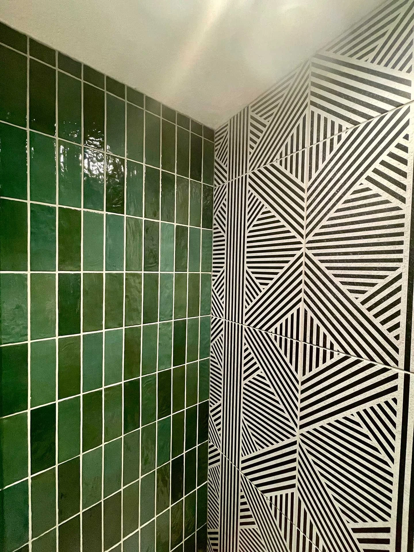 Close-up of shower tile featuring glossy green vertical subway tiles paired with bold black-and-white geometric patterned tile.