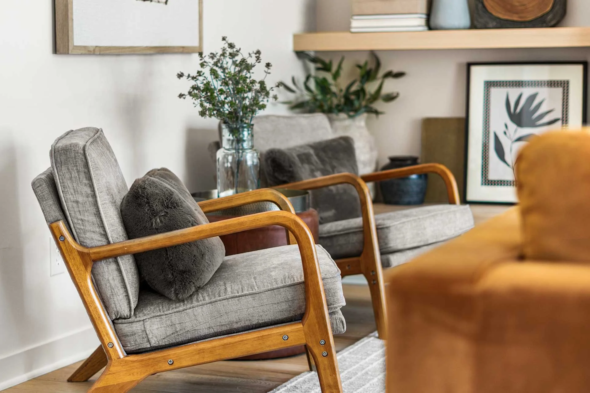 Cozy gray lounge chair with wooden accents next to greenery-filled vase in airy space, portfolio example of full service interior design in Denver.