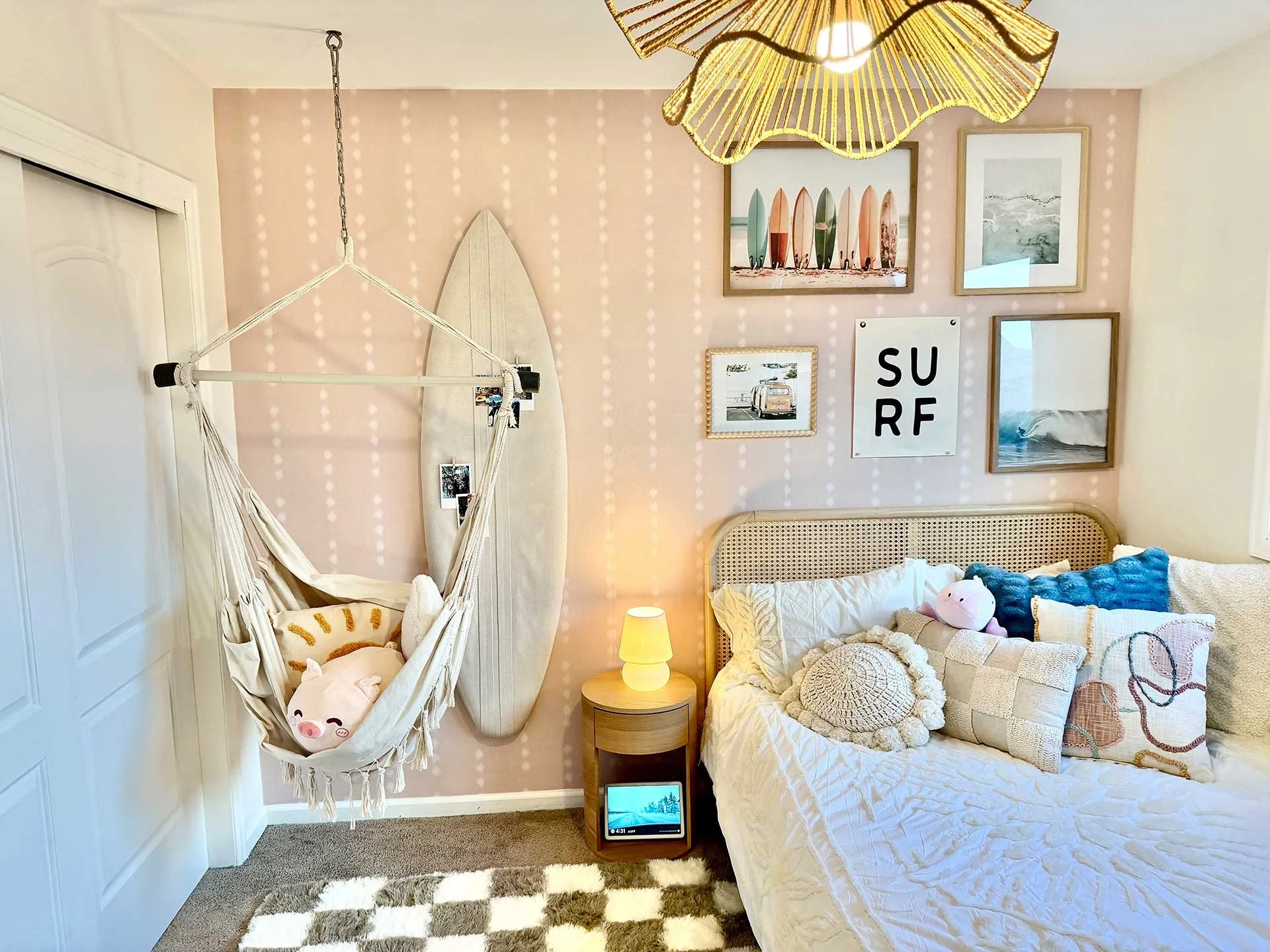 Playful pink kid's room, interior design in Denver: rattan bed, bedside lamp, hammock with toys, surfboard, and coastal framed prints.