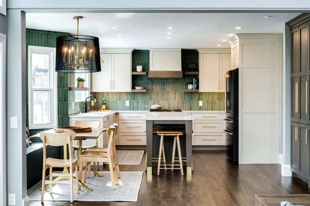Interior design in Denver portfolio piece: airy kitchen with white cabinetry, glossy green tiles, farmhouse sink, wood chairs at table, and hanging black light fixture.