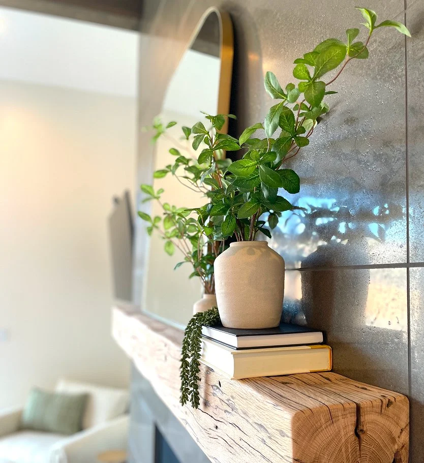 Greenery in a large ceramic vase beside a tall arched mirror on a reclaimed wood mantel  after interior design services
