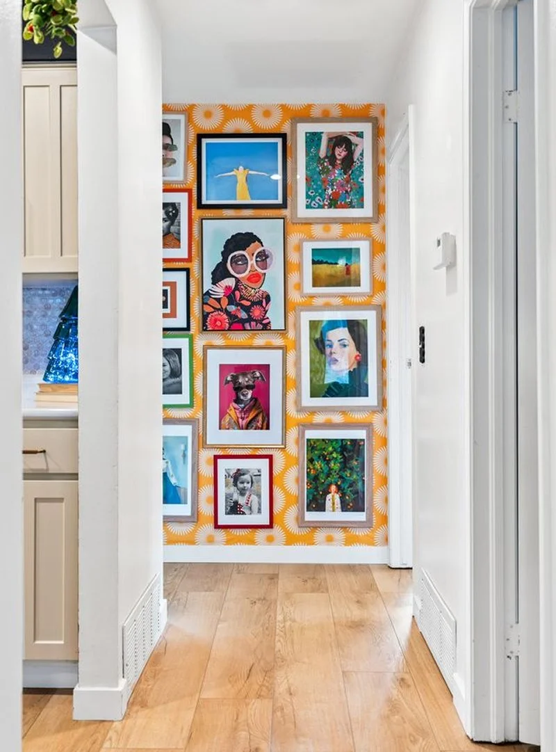 Vibrant hallway with orange polka-dot wallpaper and eclectic framed art gallery wall, put together by a Denver interior designer.