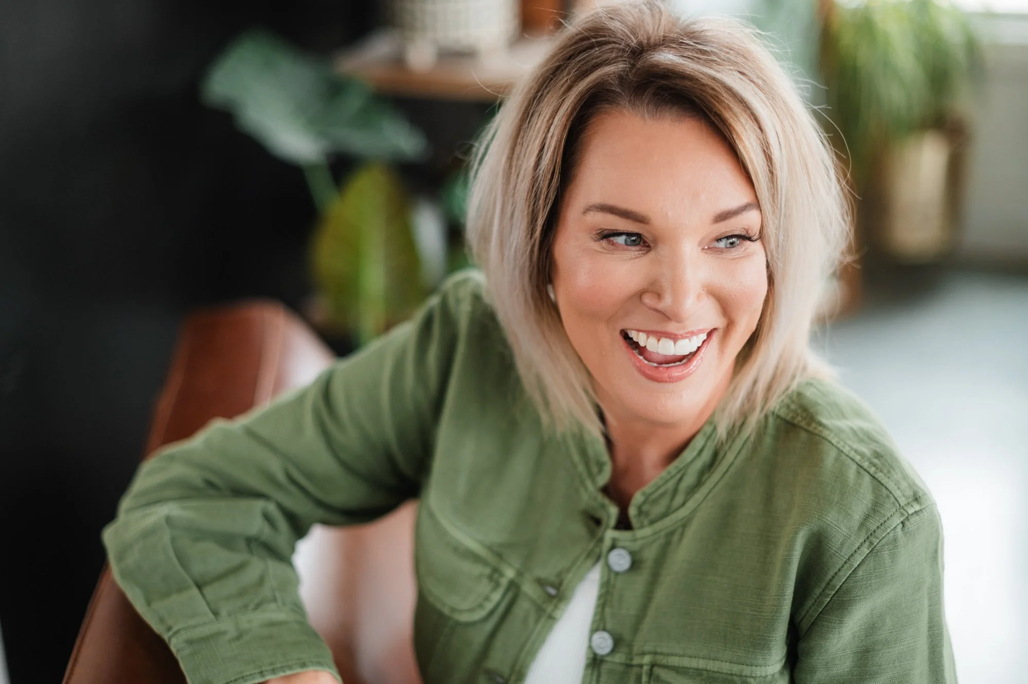 A woman with short blonde hair smiling and looking to the side, wearing a green jacket.