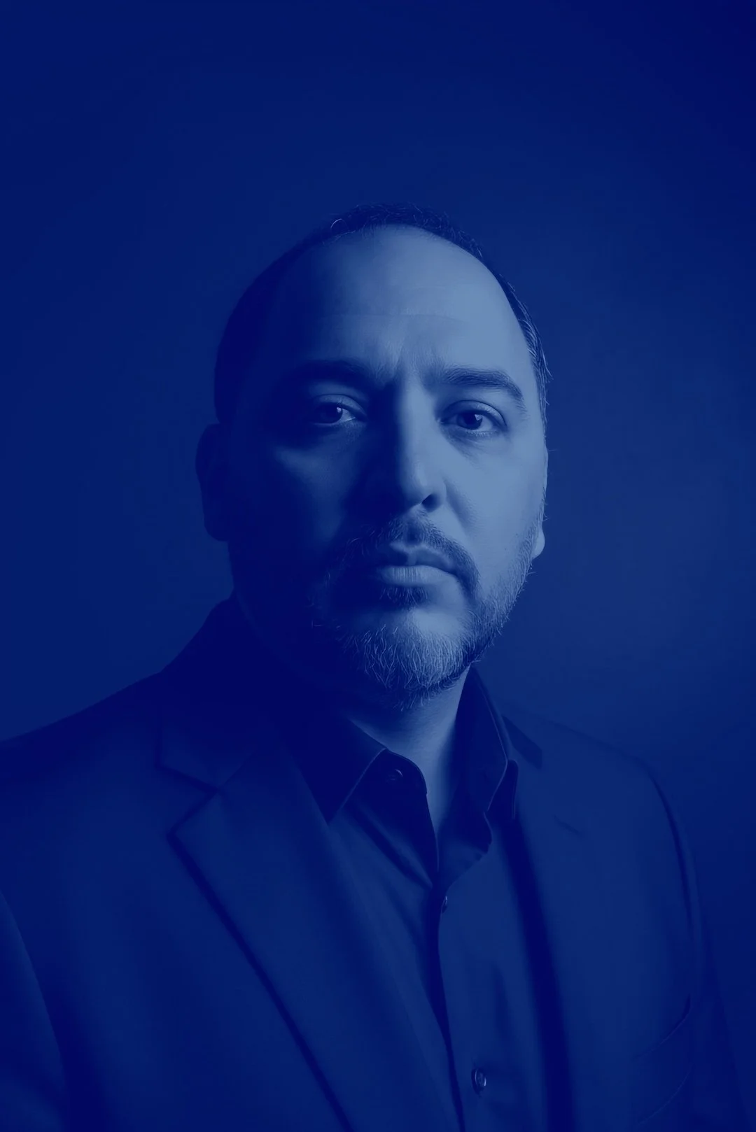 A smiling man with dark hair, wearing a dark shirt, against a blue background. Headshot of Andre Baruffi.