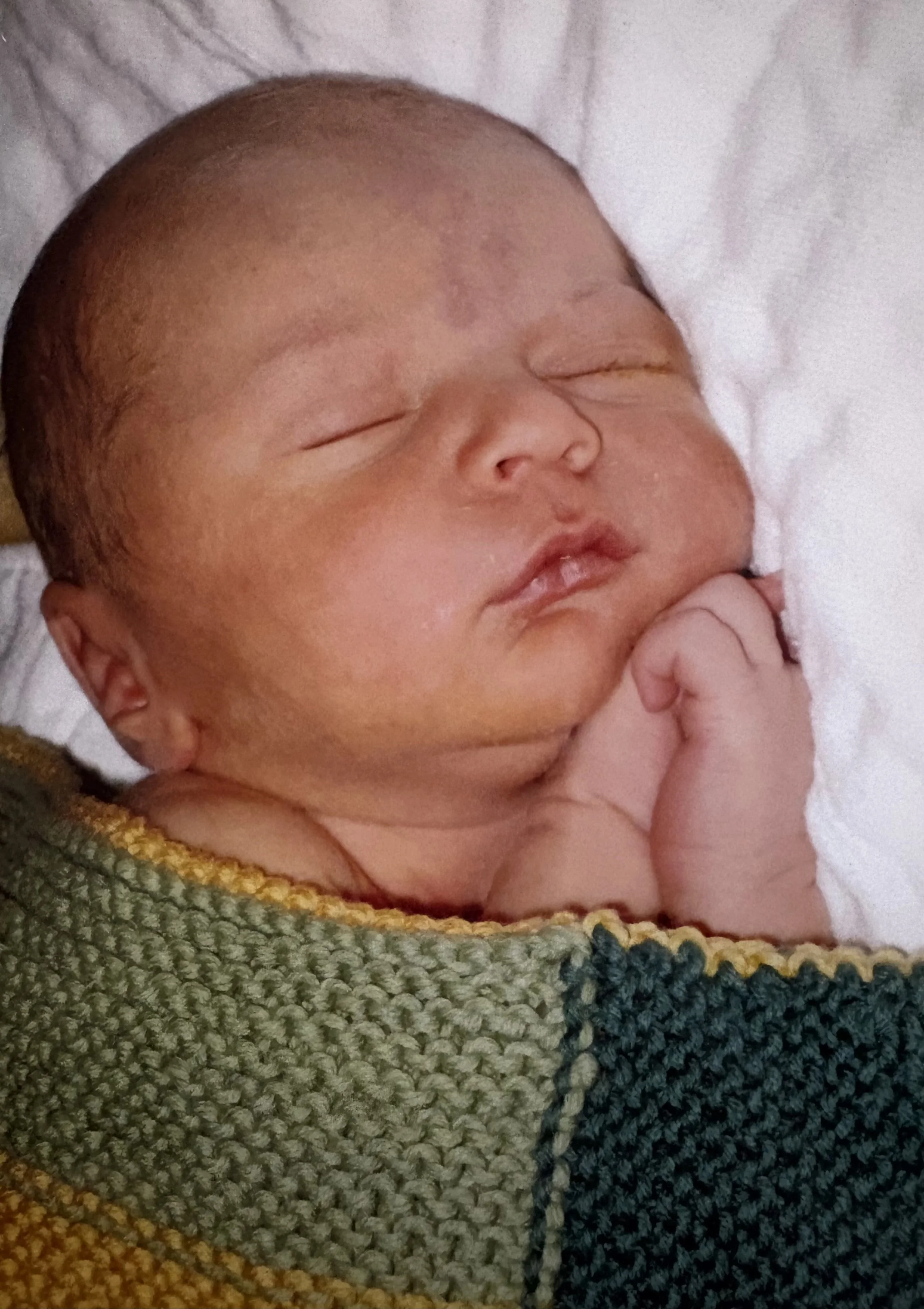 newborn sleeping baby wrapped in a green hand knit blanket