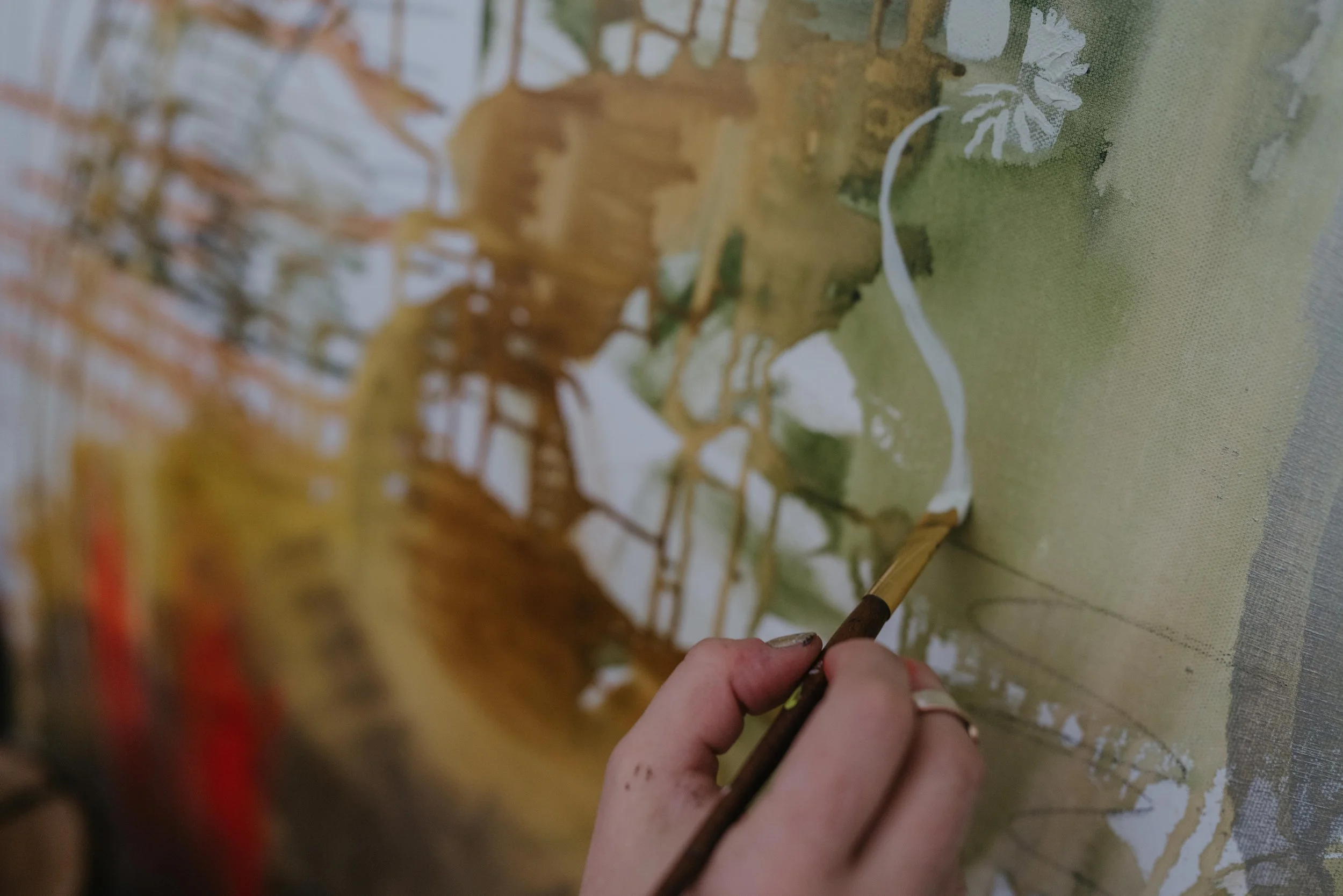 Large paining in the background; in the foreground a hand holding a paintbrush adding a white  curving line to the painting