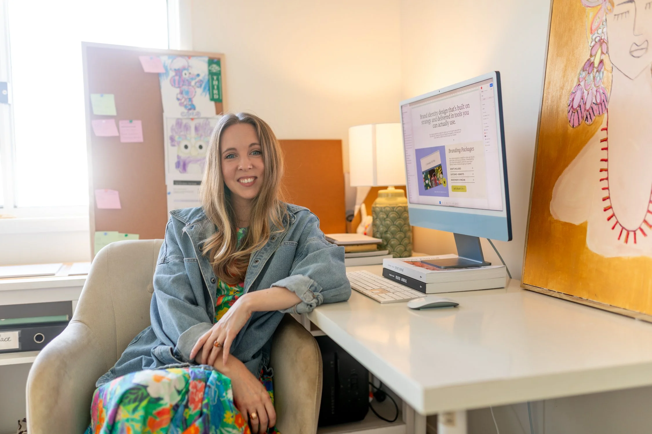 Photo of brand designer Katie Emslie sitting at her desk smiling at the camera.