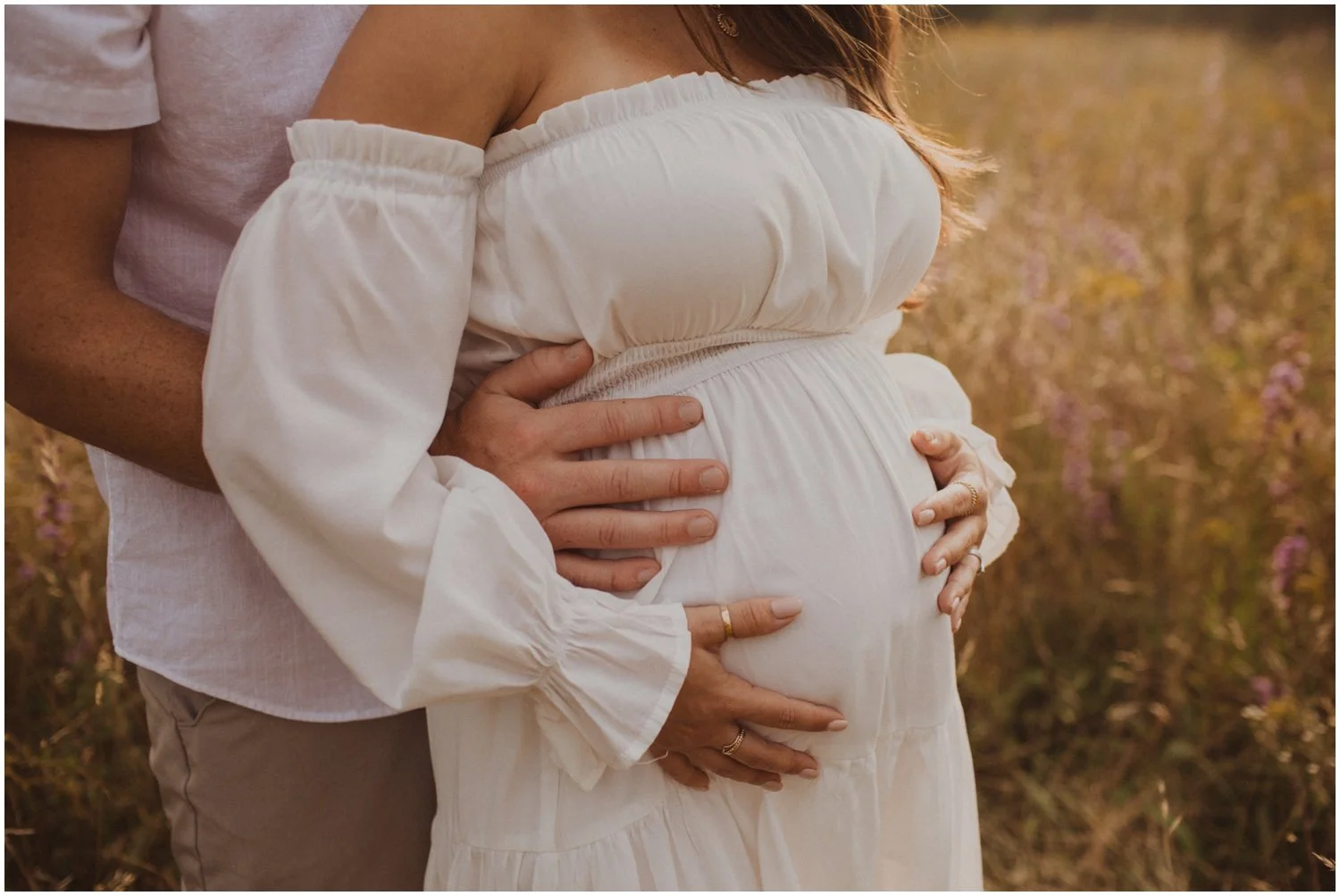 close up of pregnant belly couple is wearing white and standing in field of flowers for maternity session in wisconsin rapids