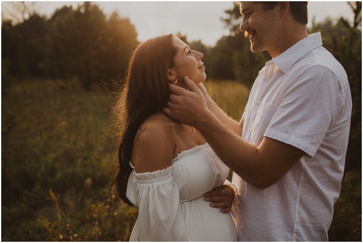 a pregnant woman in a white dress faces husband who touches her face in a field of wildflowers in a field of wildflowers in wisconsin rapids