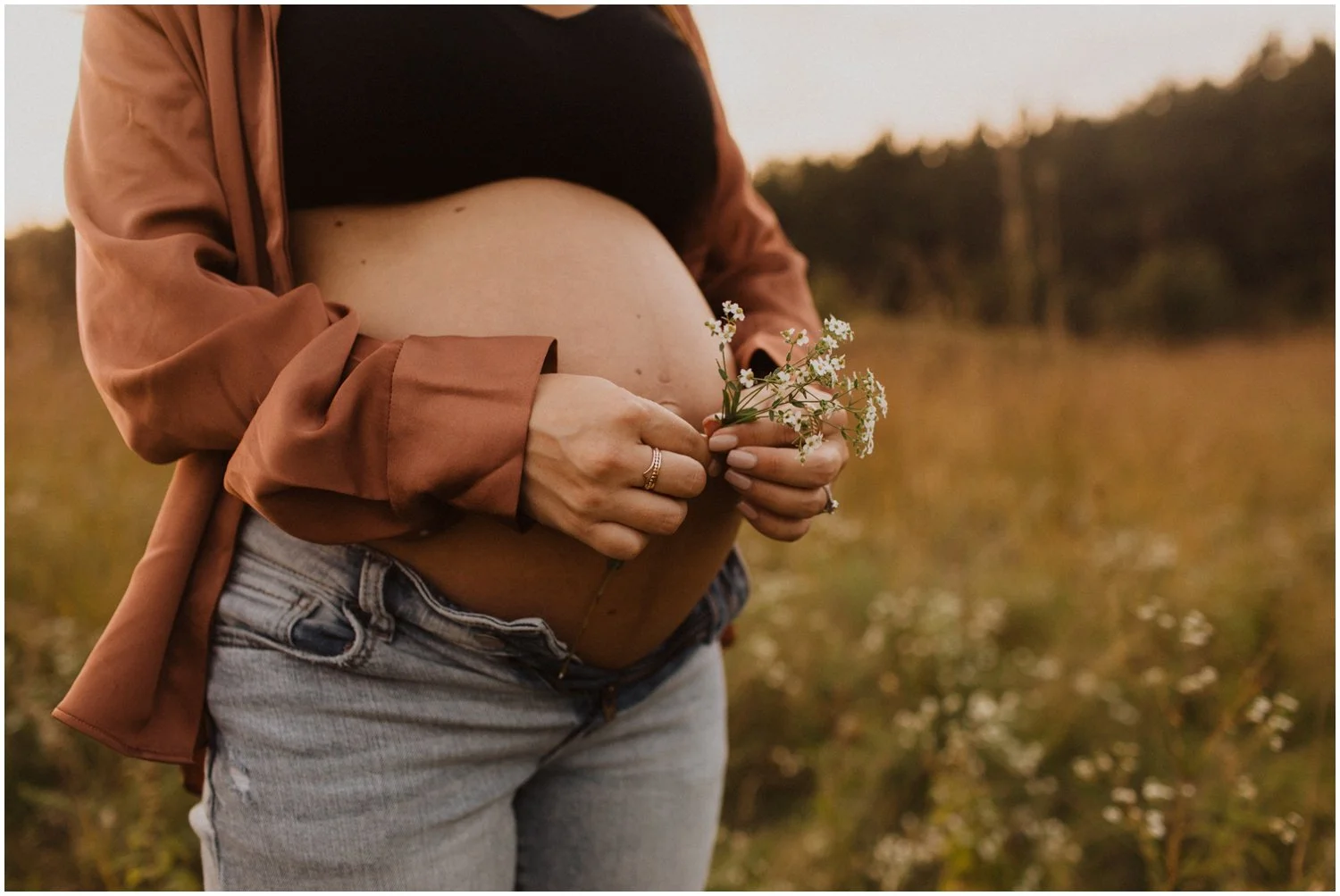 close up of woman holding white flowers in front of pregnant belly  for maternity session in wisconsin rapids