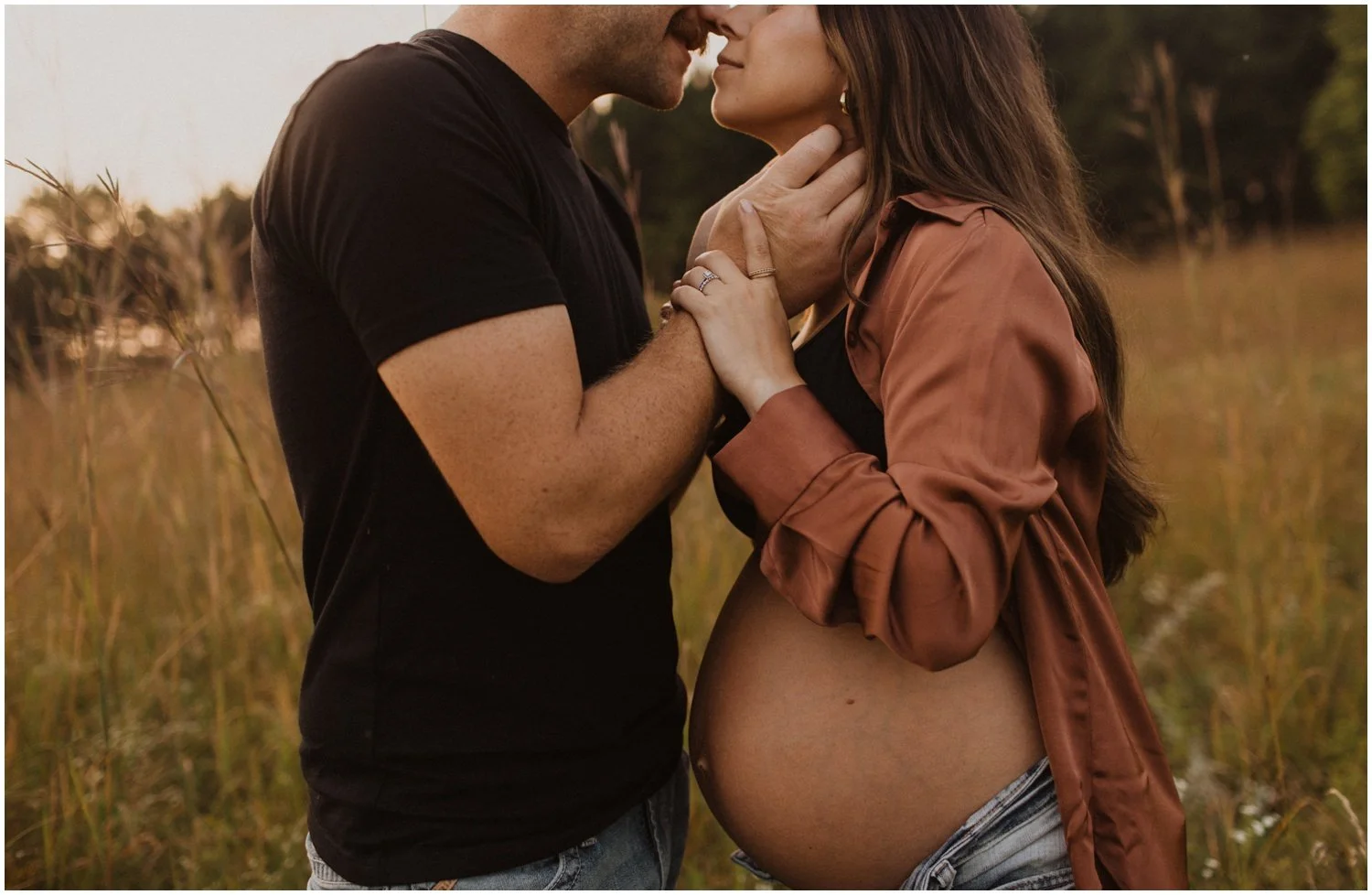 close up of pregnant woman and husband kissing in a field of long grass during golden hour in wisconsin rapids