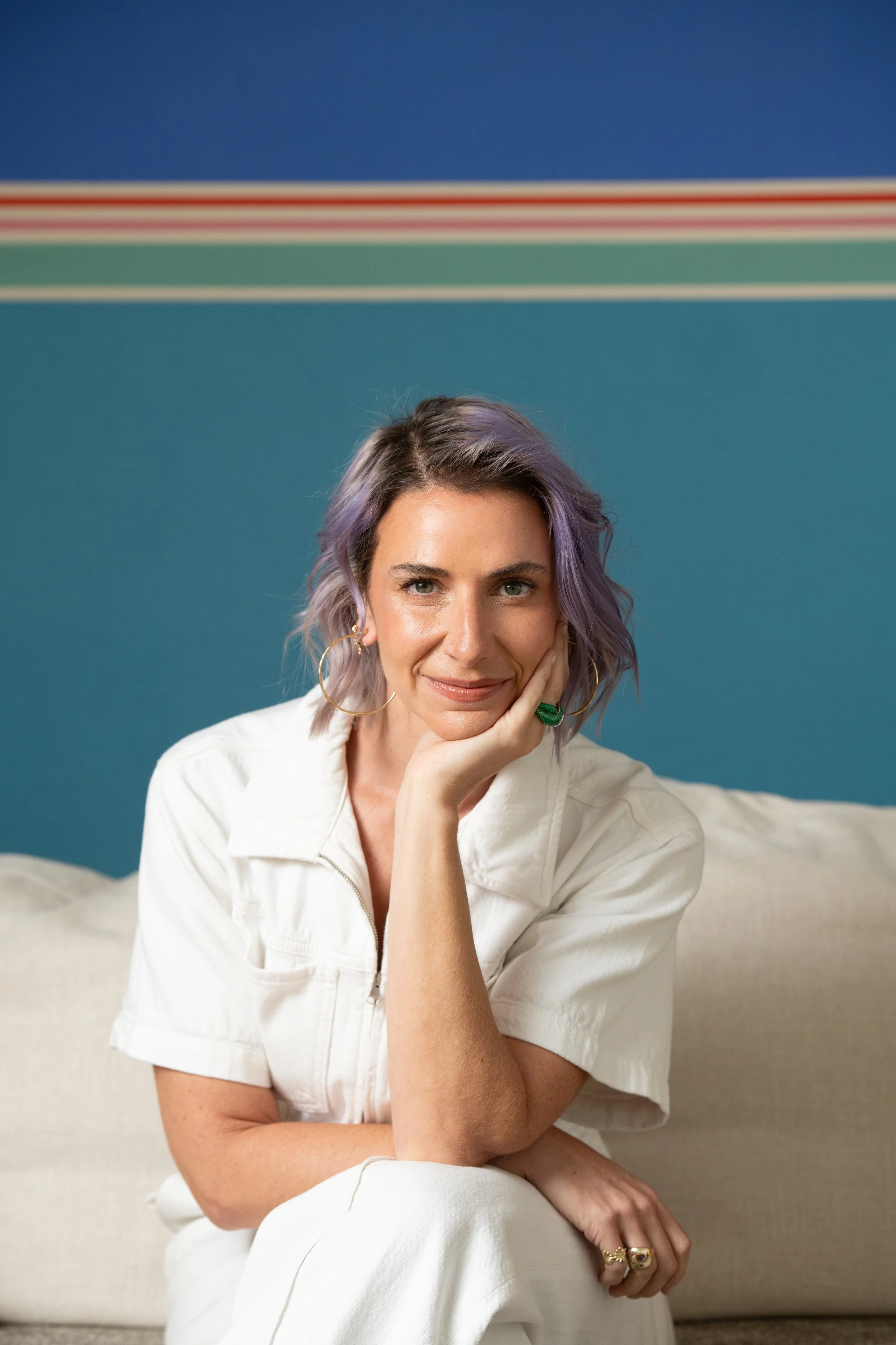 Emily sits on white couch, looking at camera.