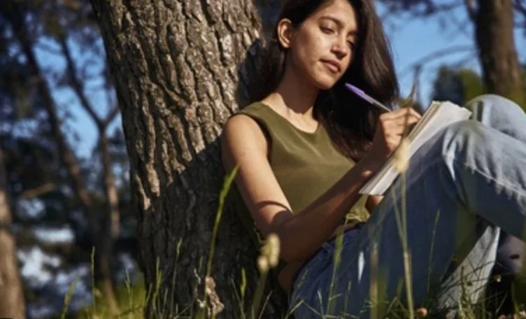 Adult woman journaling in nature as part of therapy for cultural and intergenerational healing and self-reflection.
