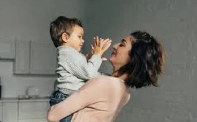 Parent holding and smiling at young child during a calm moment at home. Reflects connection, emotional support, and parenting challenges.