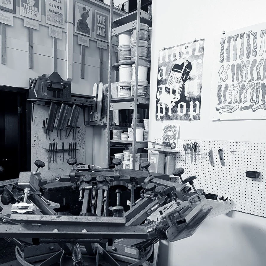 Studio Image of a T-shirt Press in a shared studio space with printmaking tools and posters hung on the wall