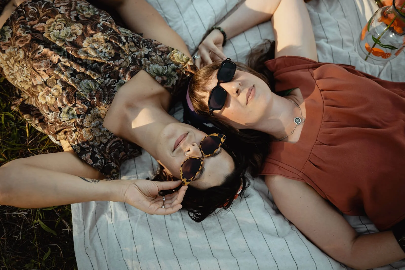 Two women are lying on a blanket outdoors, wearing Diane tops and plant dyed shibori bandanas.