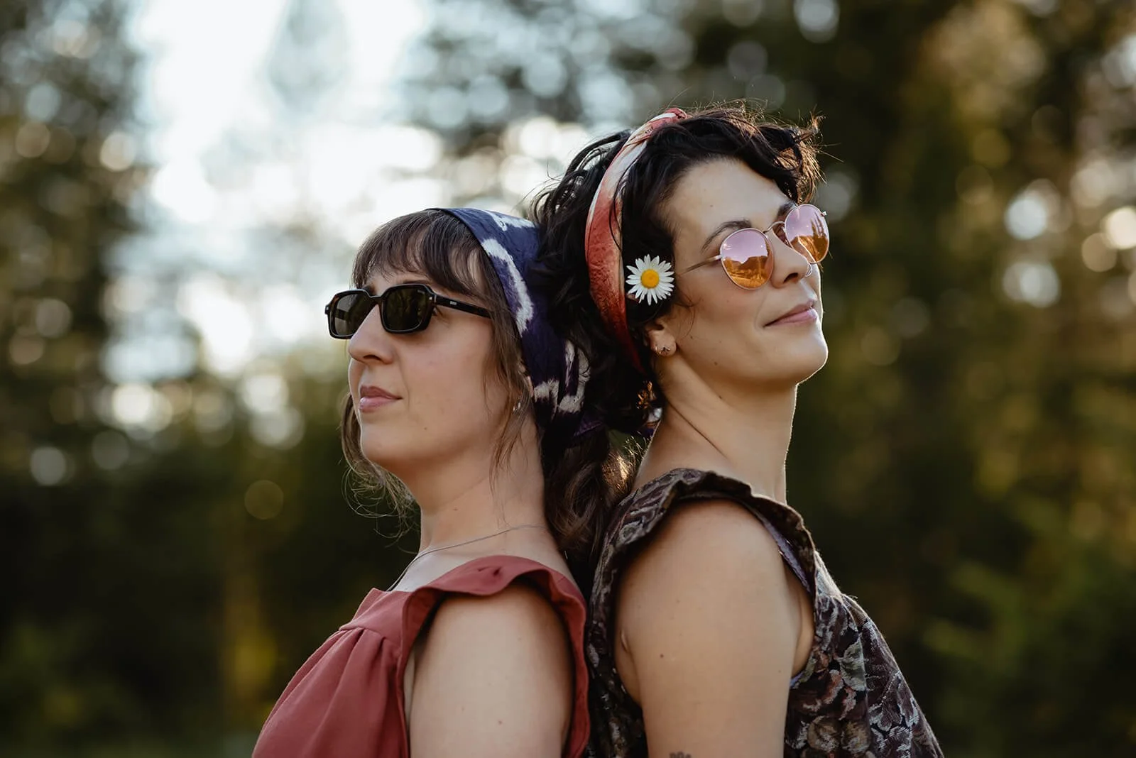 Two women standing back to back outdoors, wearing sunglasses the Diane tops and plant dyed bandanas in their hair