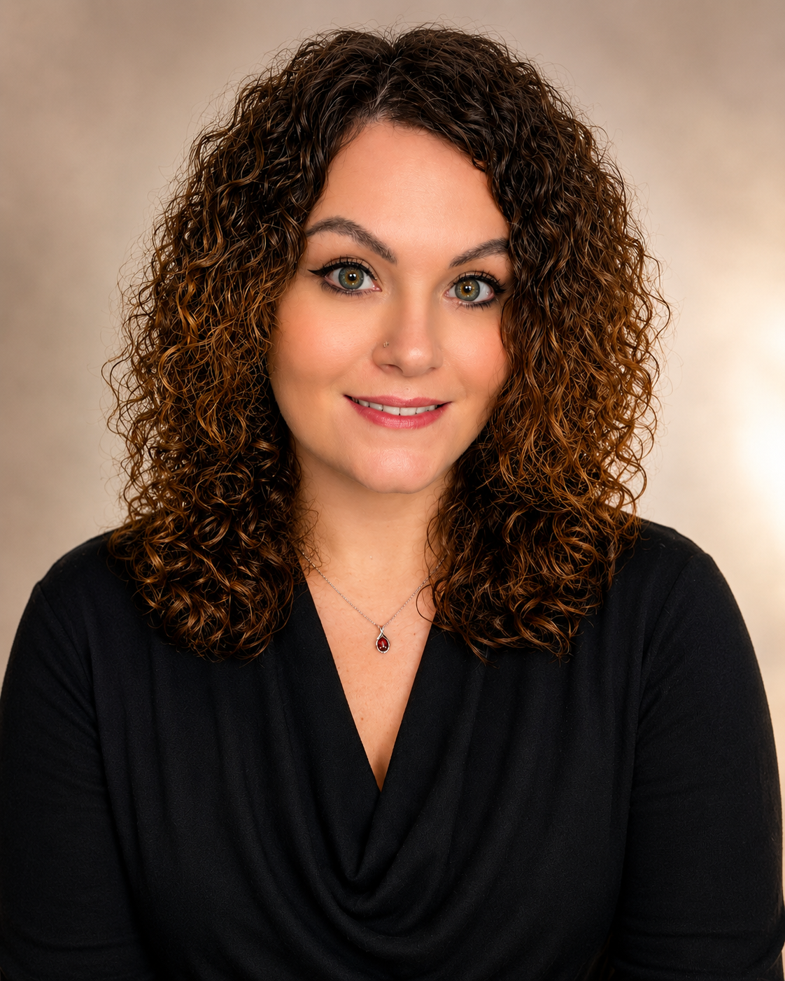 A woman with curly brown hair, wearing a black top and necklace, smiling at the camera.