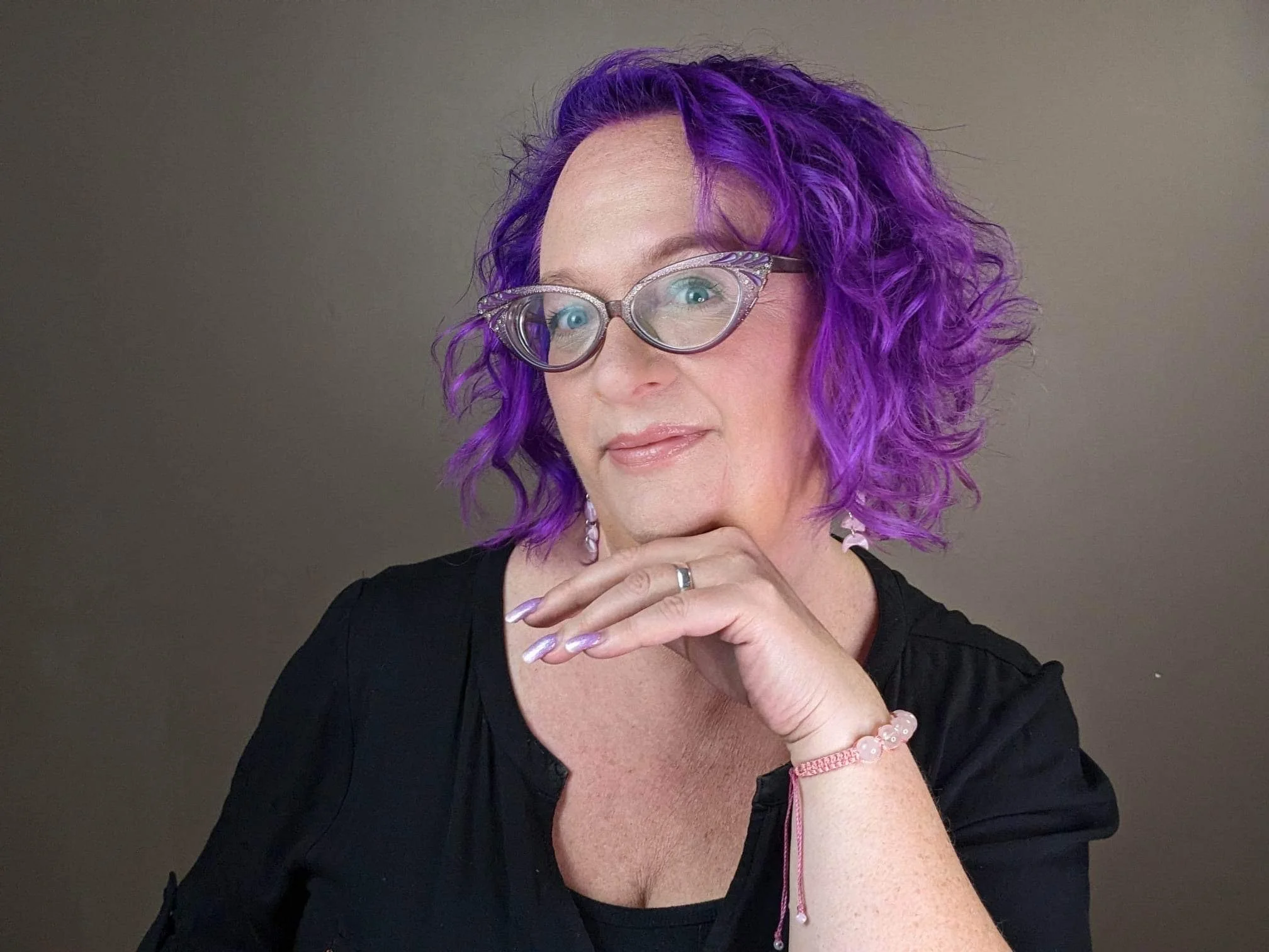 Rachel rests her head on her hand - she is trying desperately to bring this pose back! Her short hair is bright purple and matches her sparkly cats-eye glasses.