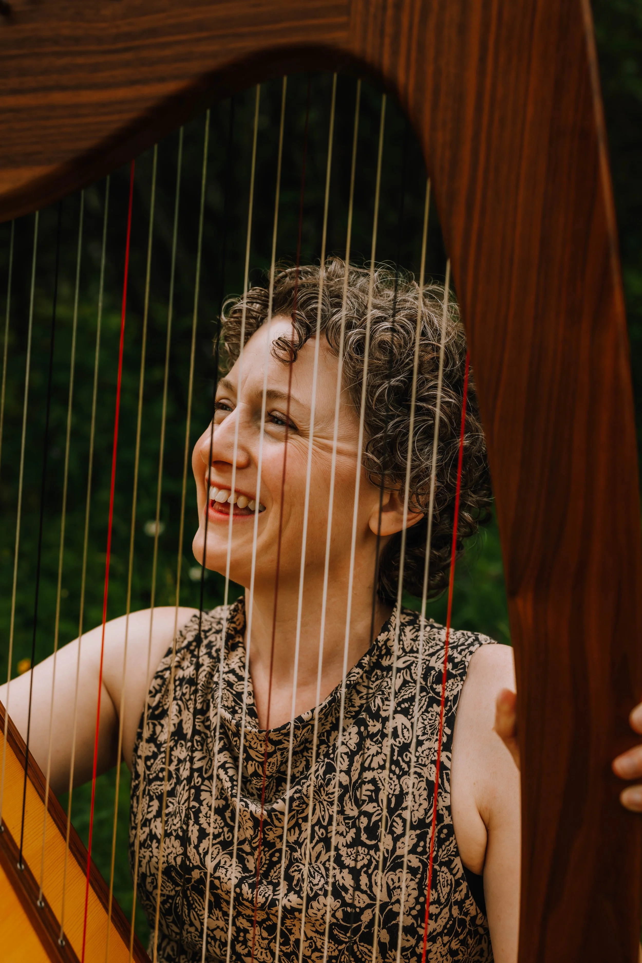Olivia smiles through her harp's strings, which Fram her face and patterned black and beige sleeveless dress.