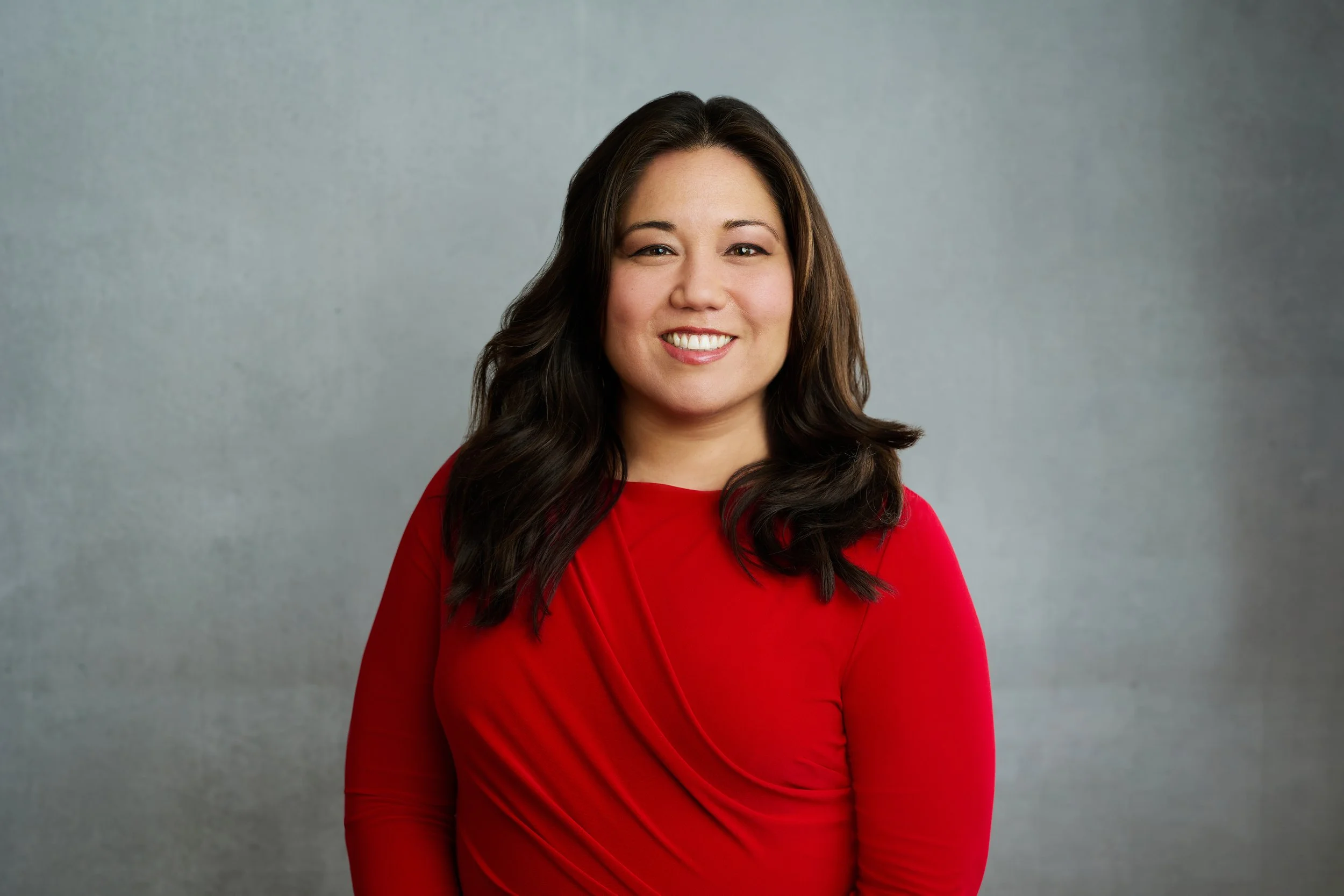 Stephanie smiles at the camera. She is wearing a red top and her long, auburn hair is loose around her shoulders.