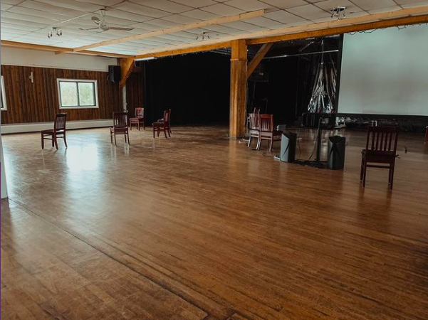 A large room for rehearsals, empty except for a few scattered chairs.