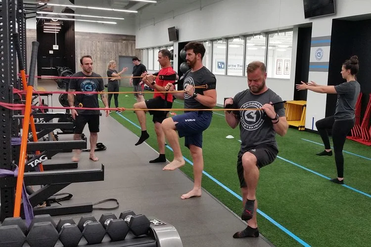 People wearing athletic gear participating in a group fitness class focusing on balance and coordination, using resistance bands and balance exercises in a gym.